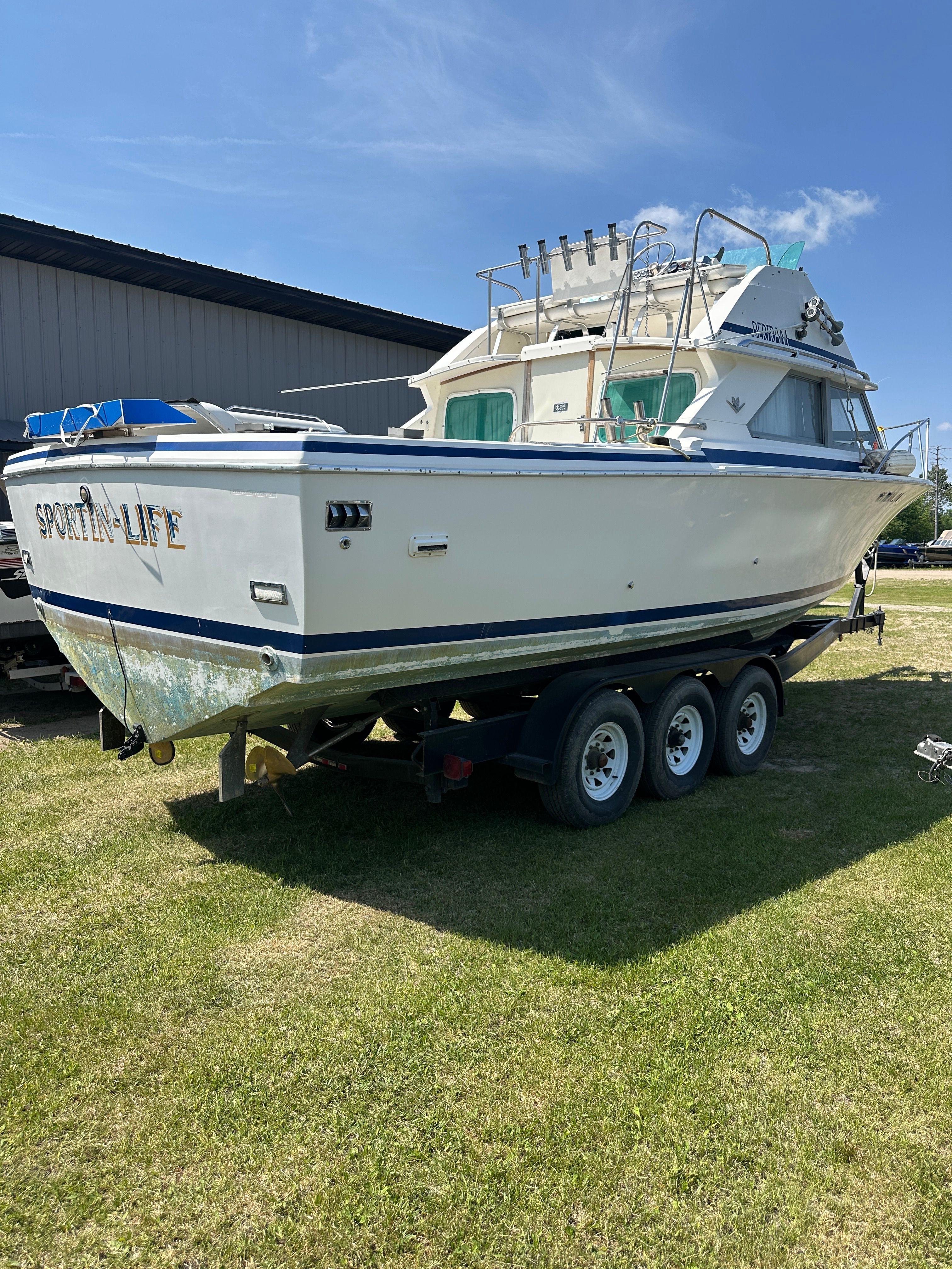 A 1983 Bertram Flybridge Cruiser on a trailer, parked on grass.