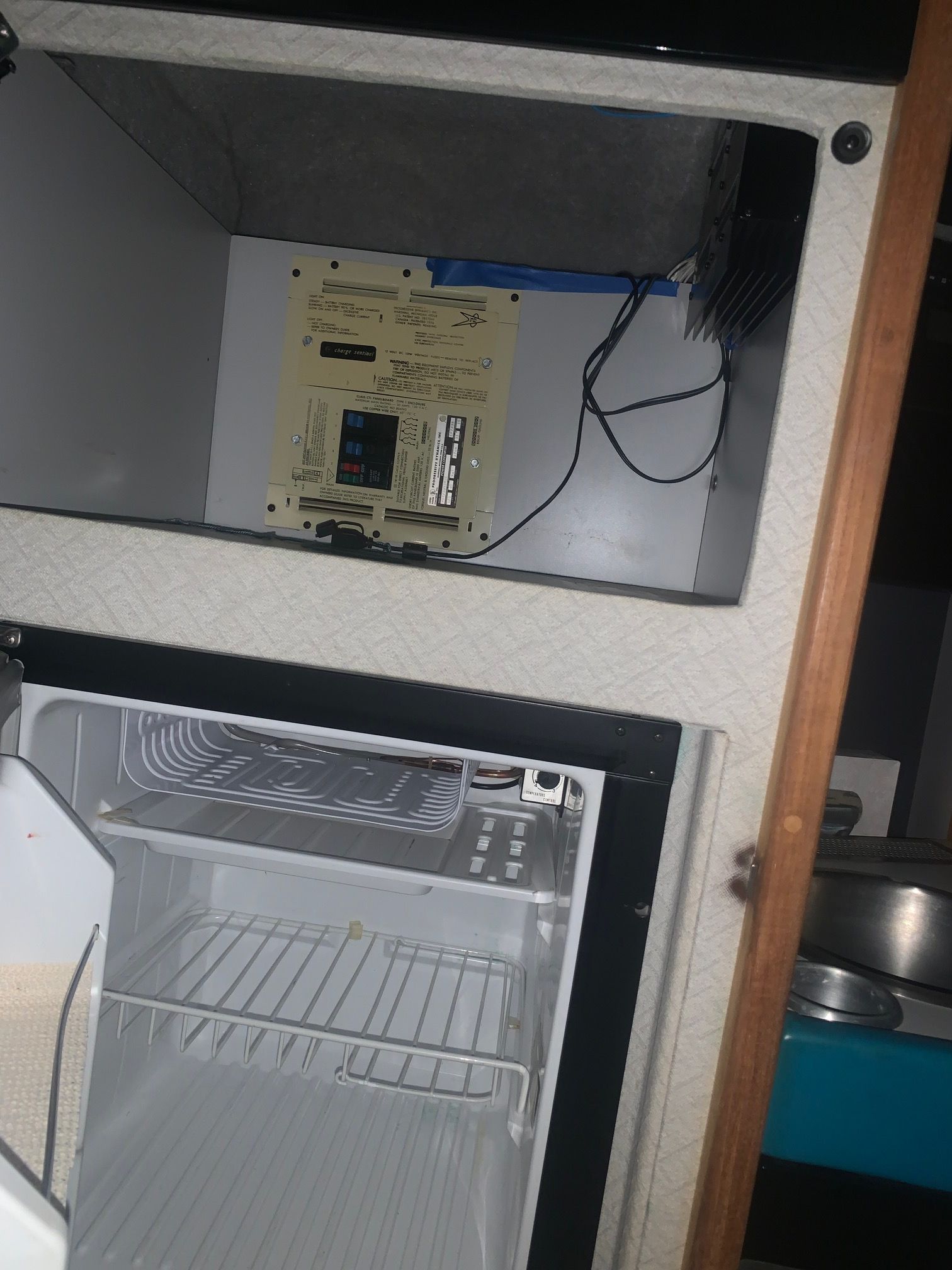 An open refrigerator in a boat with visible wires and a control panel.