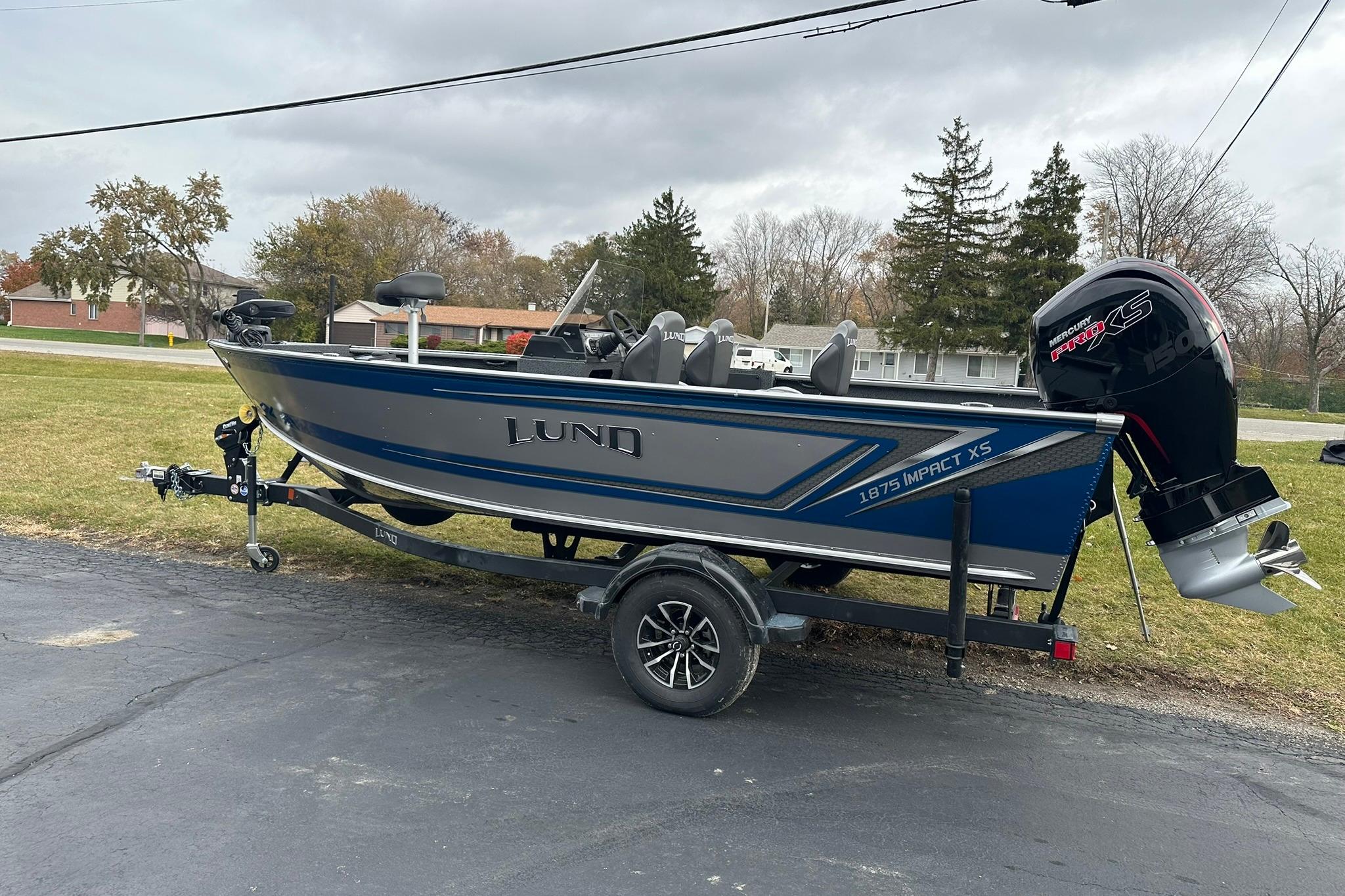 2026 Lund 1875 Impact XS SS boat on trailer, parked outdoors on a cloudy day.