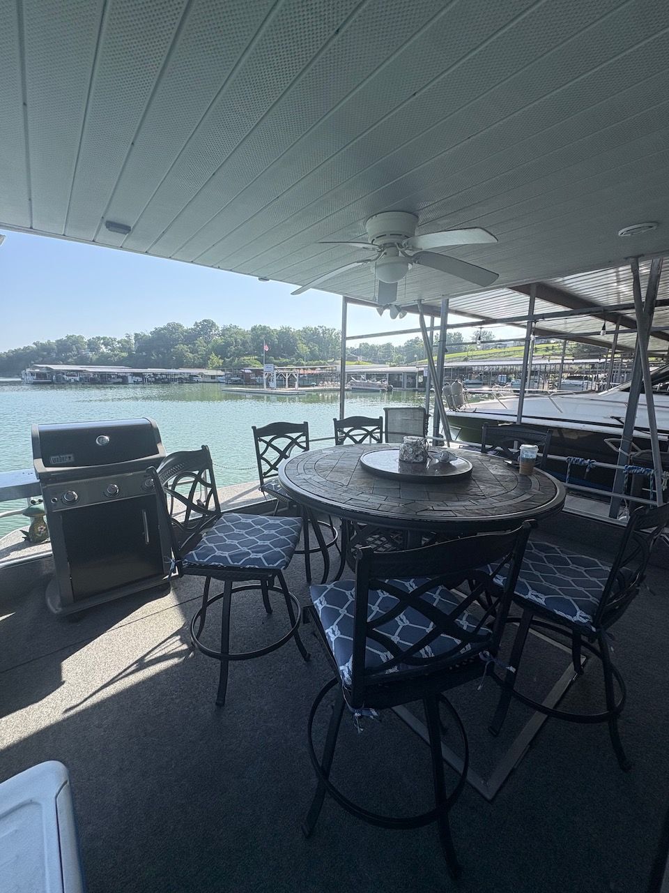 A cozy outdoor area on a houseboat with table, chairs, and grill, surrounded by water.