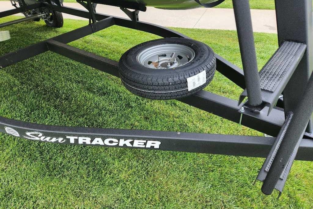 2026 Sun Tracker Party Barge 20 DLX trailer with spare tire on grass.