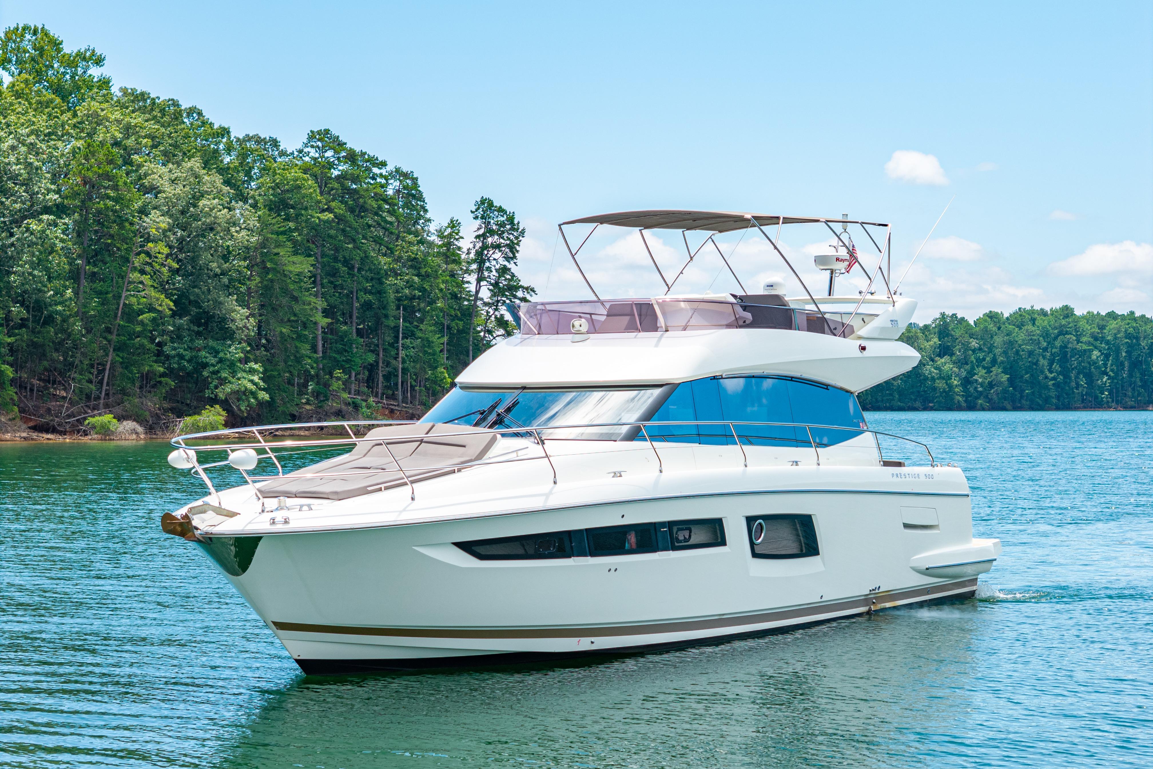 Luxurious 2017 Prestige 500 yacht cruising on a serene lake with lush green forest backdrop.