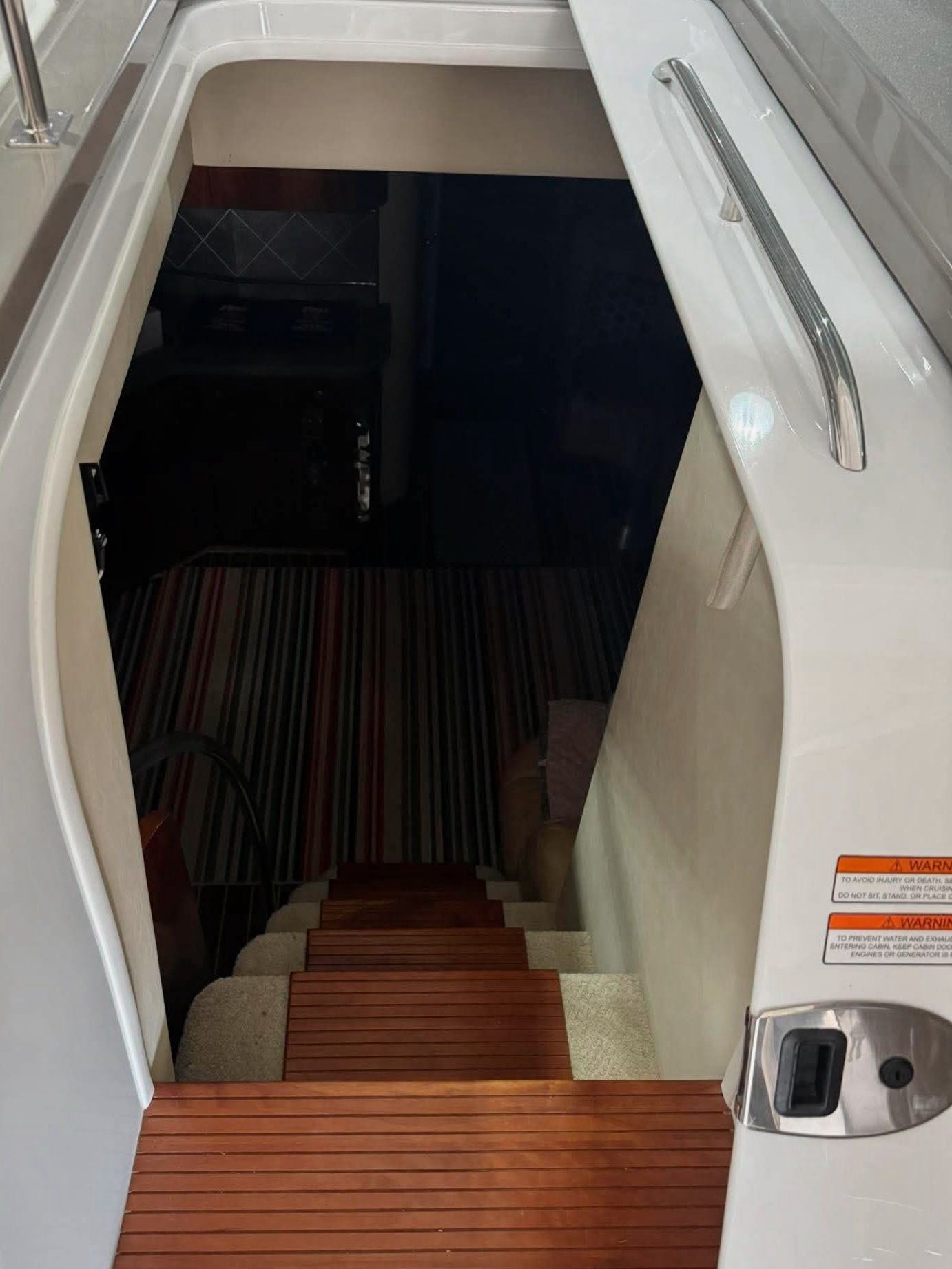 Staircase with wooden steps leading into a yacht's interior. White walls and a dark entrance.