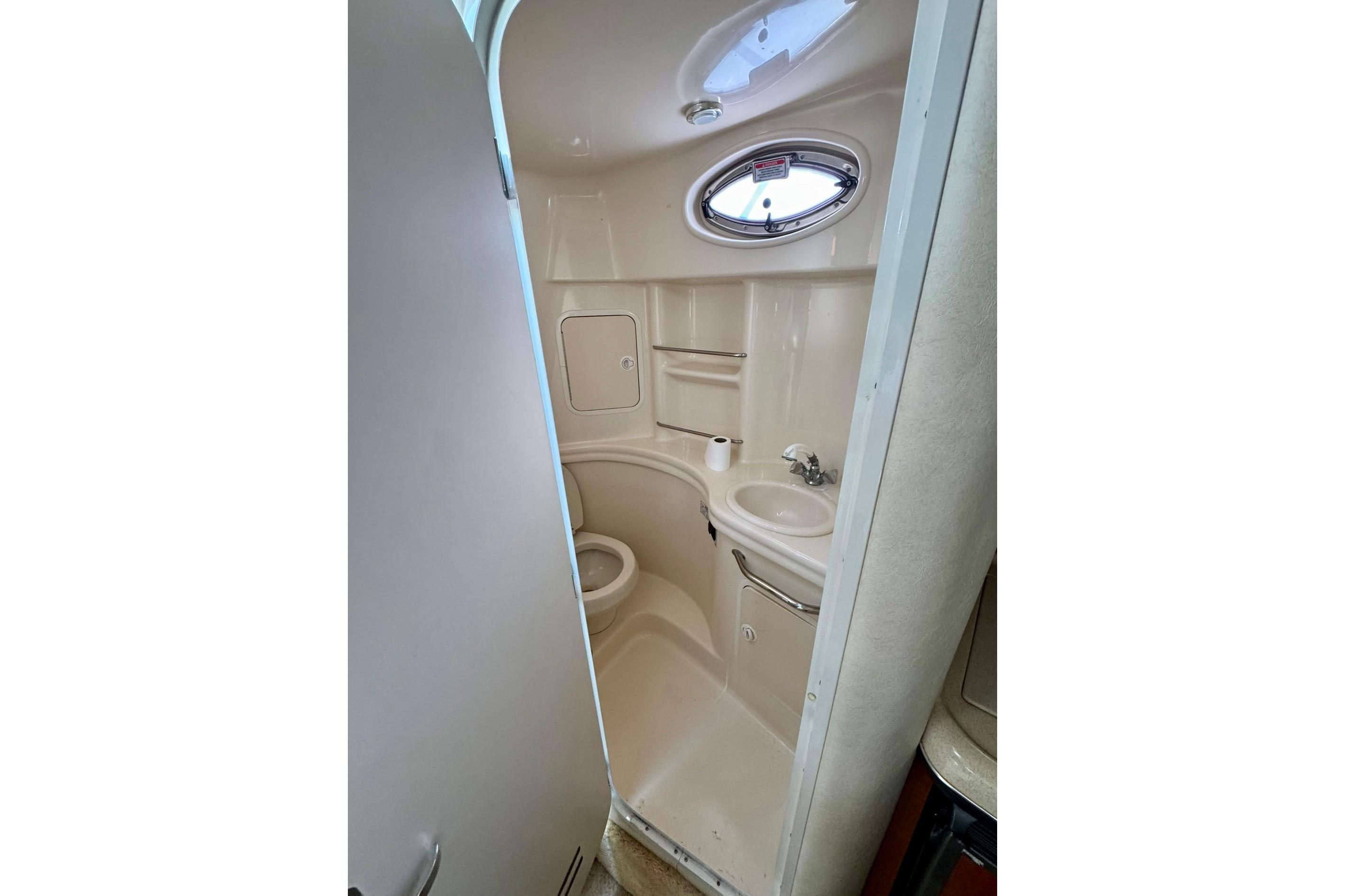 Compact bathroom in 2003 Sea Ray 300 Sundancer boat with sink, toilet, and porthole window.