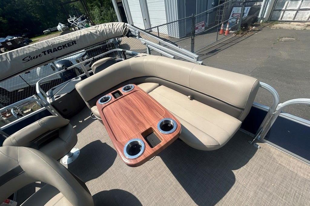 2023 Sun Tracker Bass Buggy 18 DLX pontoon boat with beige seating and wooden table.
