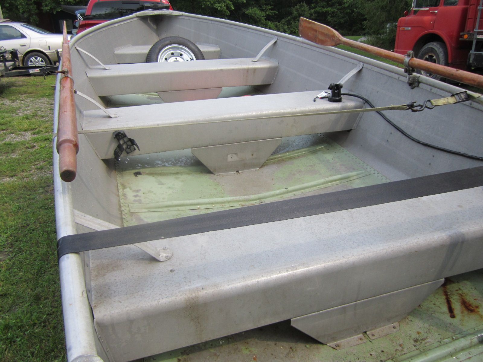 An aluminum boat with wooden oars, parked on a trailer, surrounded by vehicles.