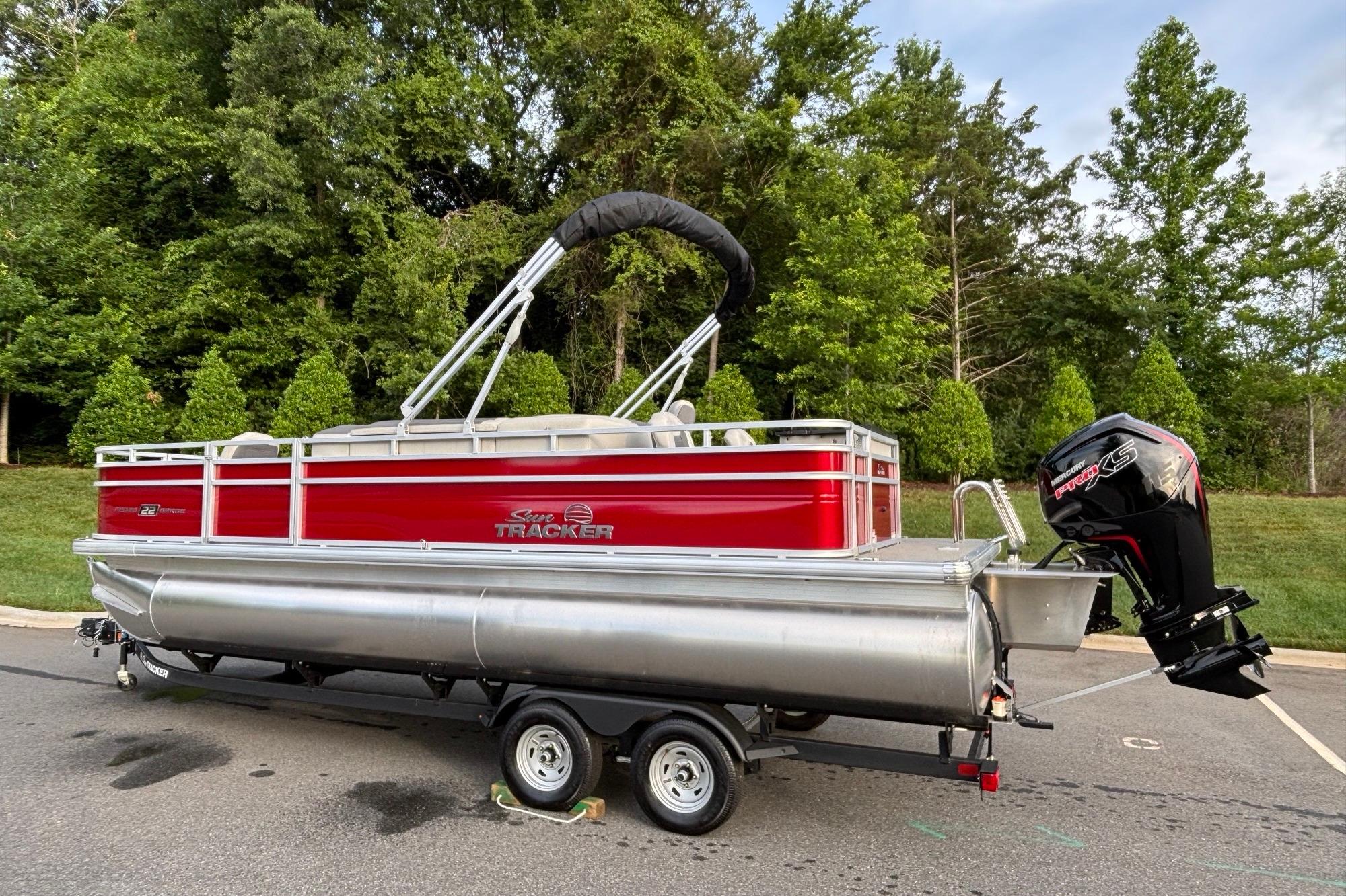 2026 Sun Tracker Fishin' Barge 22 DLX pontoon boat on trailer, parked outdoors.