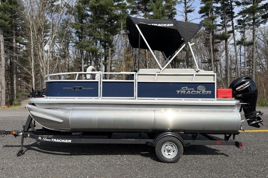 2026 Sun Tracker Bass Buggy 16 XL Select pontoon boat on trailer, parked outdoors.