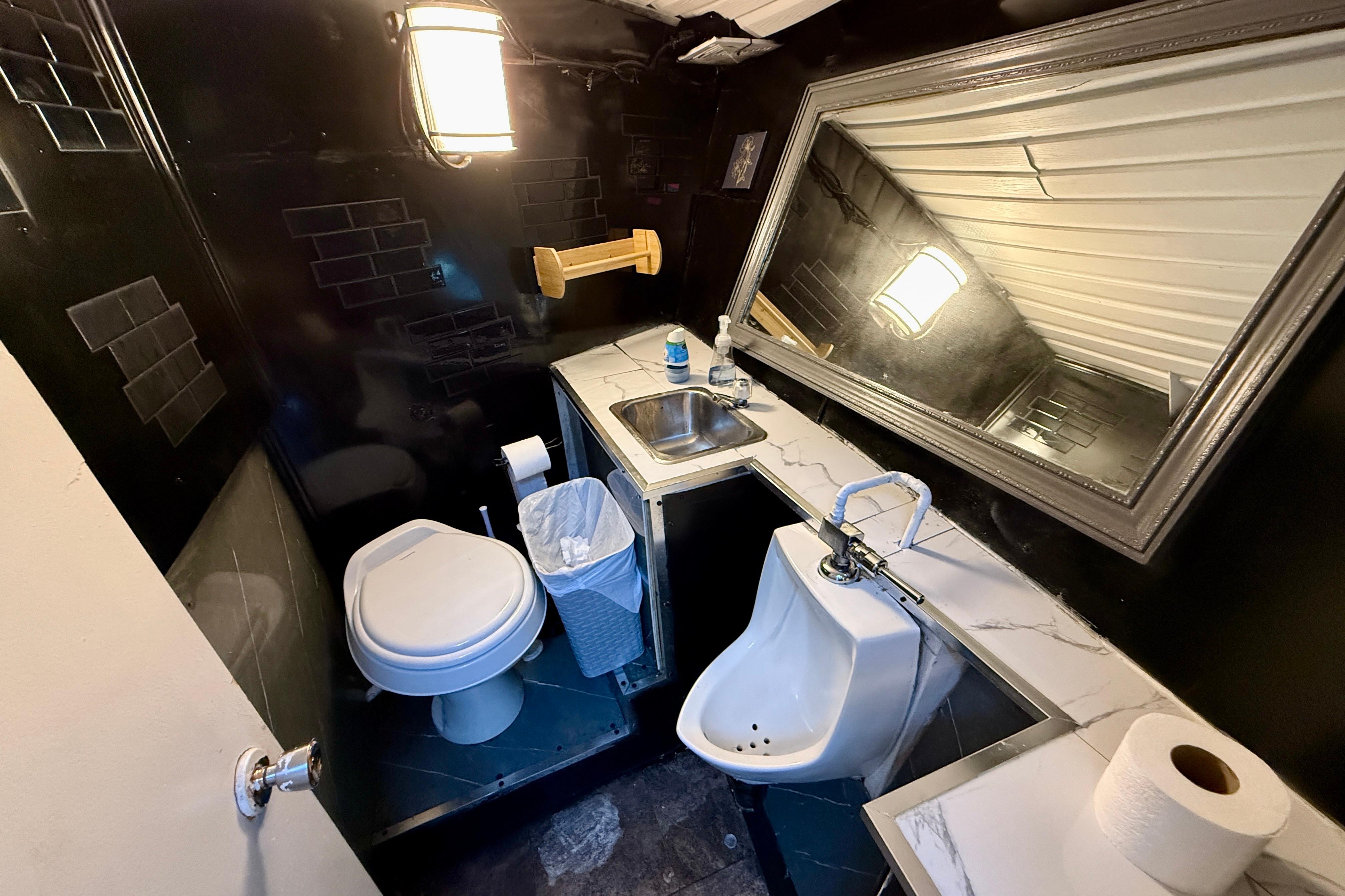 Compact bathroom with toilet, urinal, sink, and large mirror in a 1983 Custom Steel Passenger model.