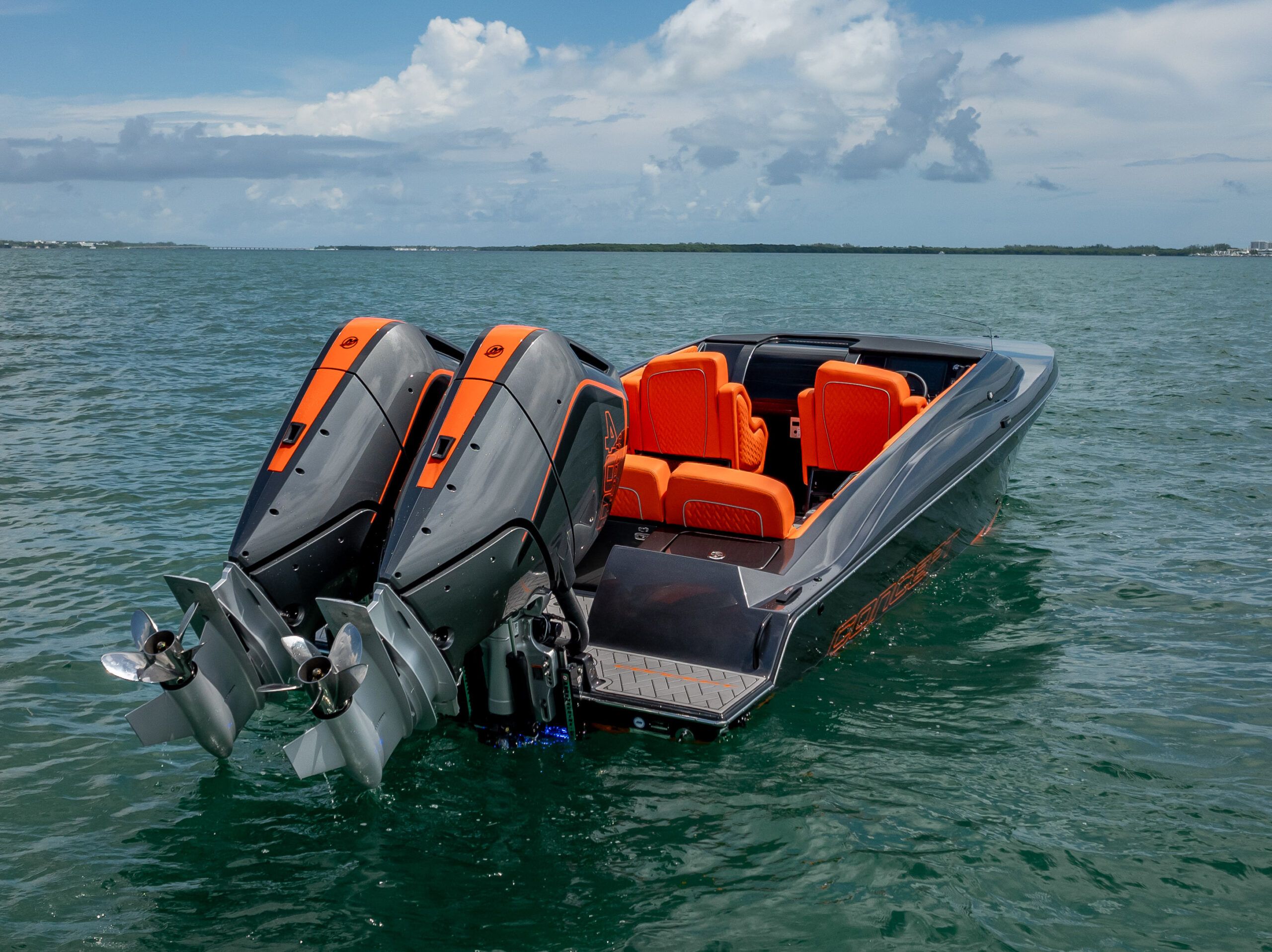 A modern sport boat with twin outboard engines and bright orange seats on calm water.
