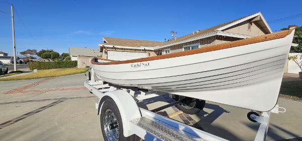 A white rowboat on a trailer in front of a house.