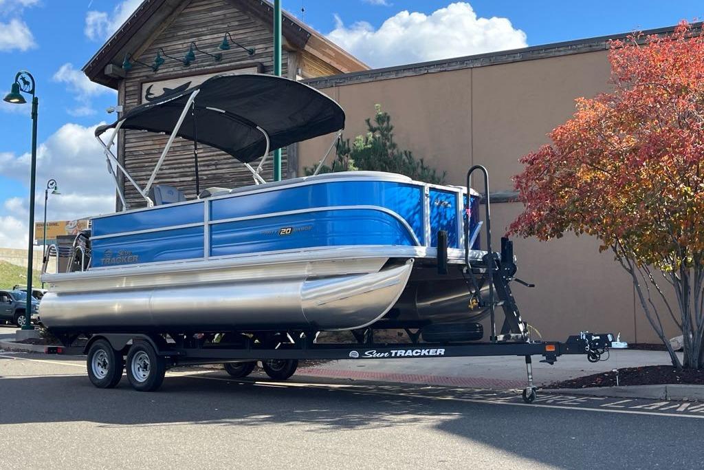 2026 Sun Tracker Party Barge 20 DLX pontoon boat on trailer, parked near building.