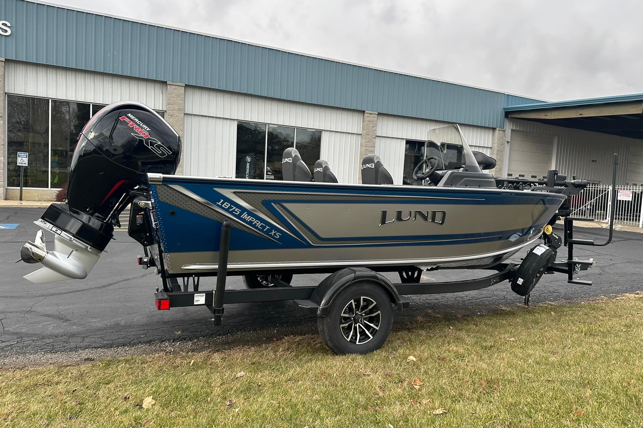 2026 Lund 1875 Impact XS SS boat on trailer, parked outside a building.