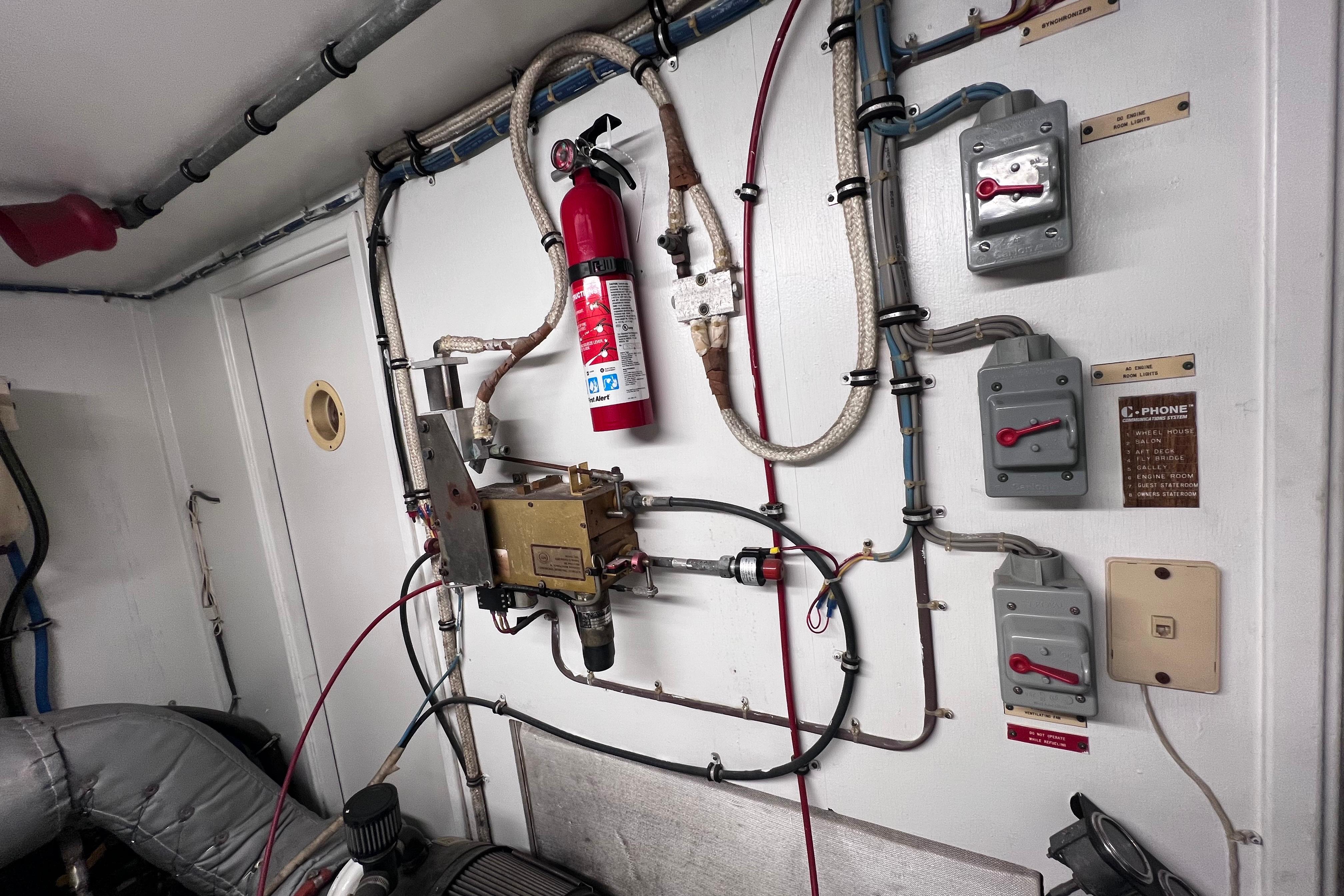 Engine room of 1987 Hatteras 70 Cockpit Motor Yacht with fire extinguisher and control panels.
