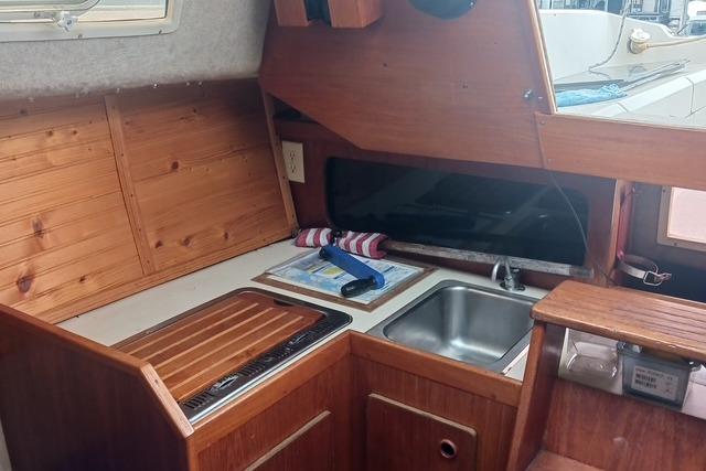 1989 O'Day 272 sailboat interior kitchen with wooden cabinetry and stainless steel sink.
