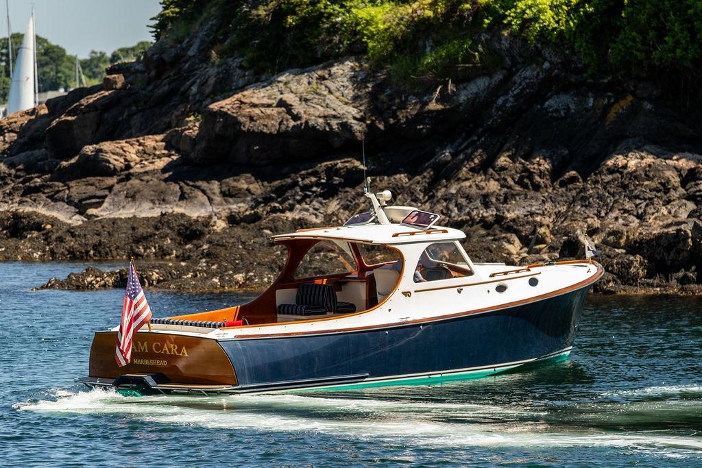Hinckley Picnic Boat 36 Classic, 2000 model, cruising near rocky shoreline with American flag.