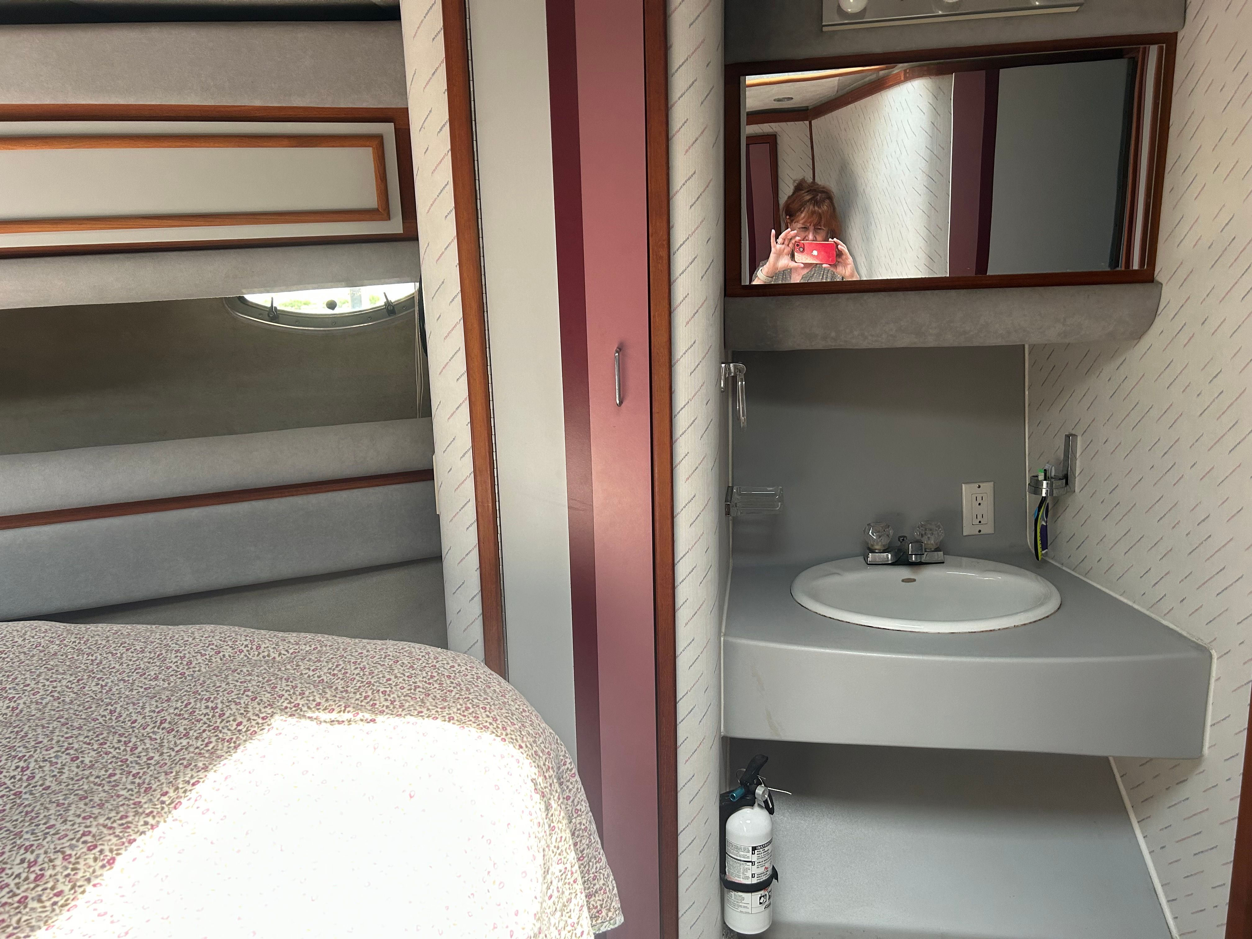 Interior of a yacht with a sink, mirror, and bed.