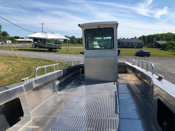A sturdy workboat with an aluminum deck and cabin, parked on dry land.