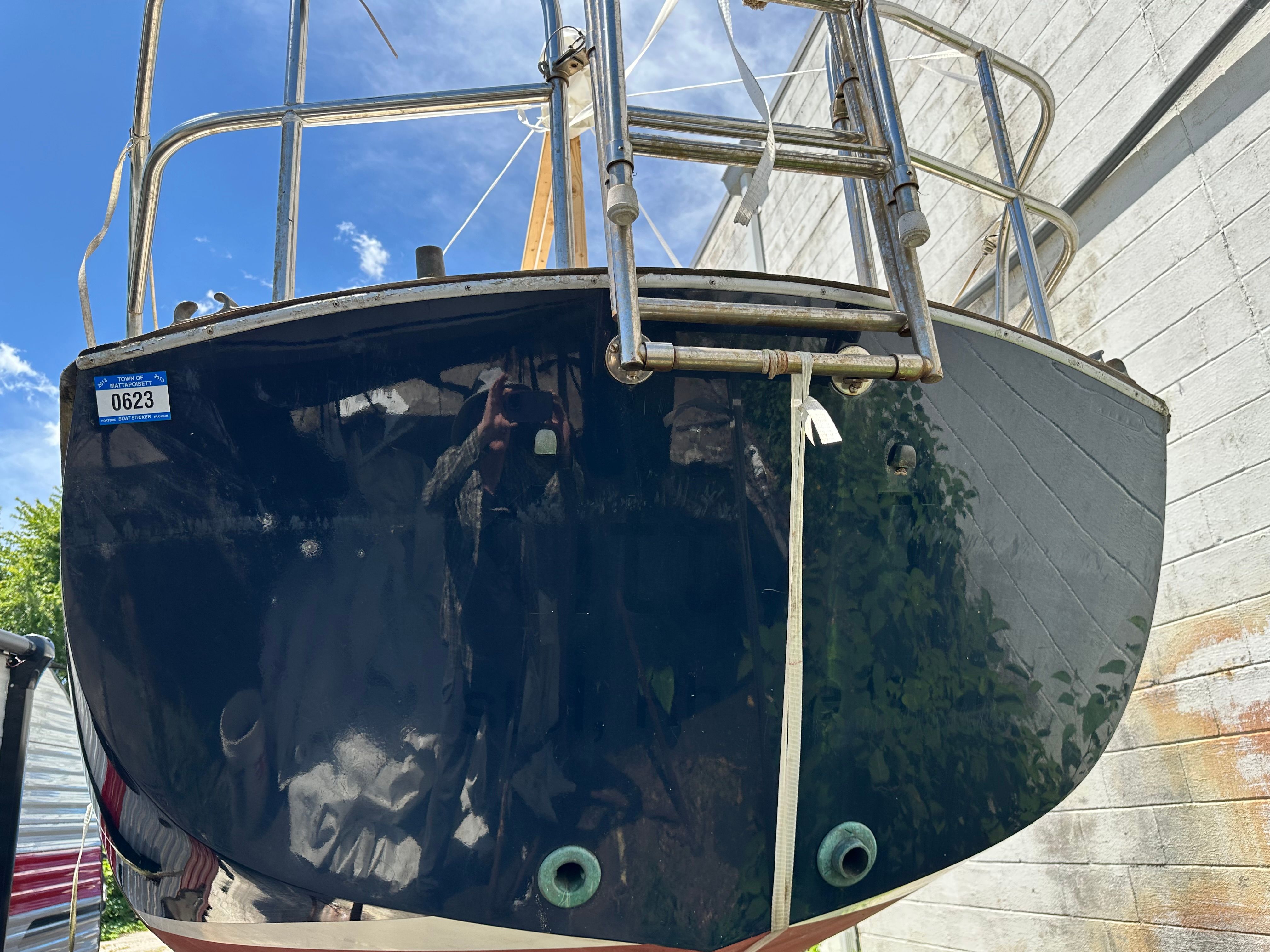 Rear view of a Cape Dory 25D sailboat with shiny hull and ladder, stored on land.