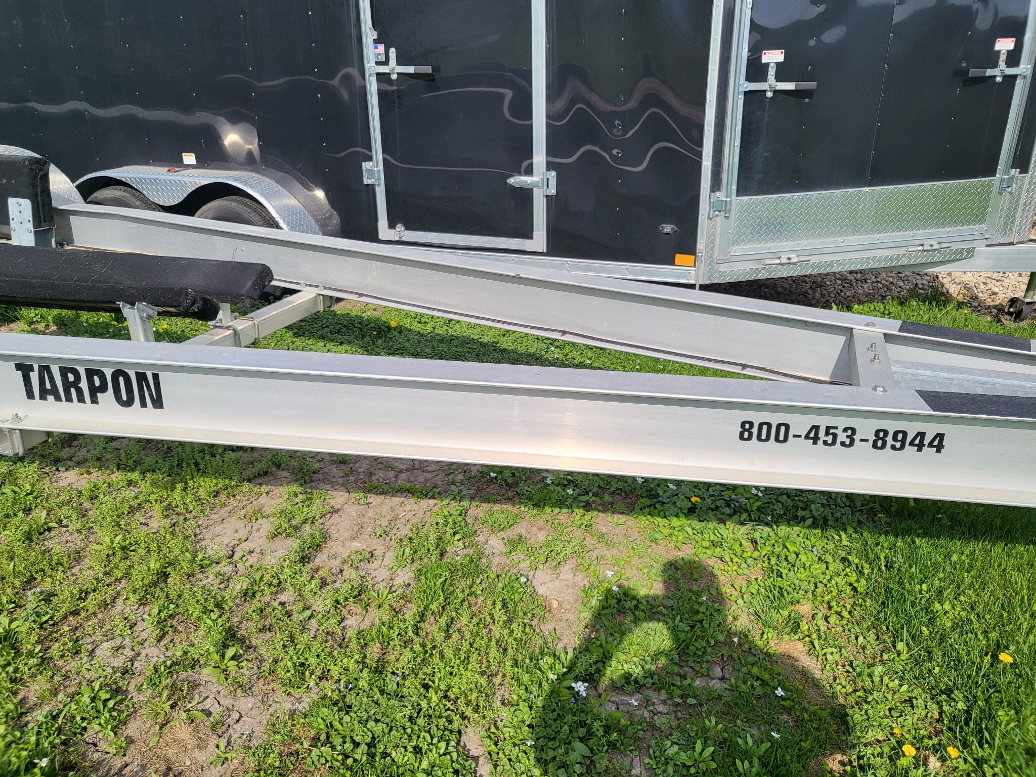 A boat trailer on grass next to a black trailer.