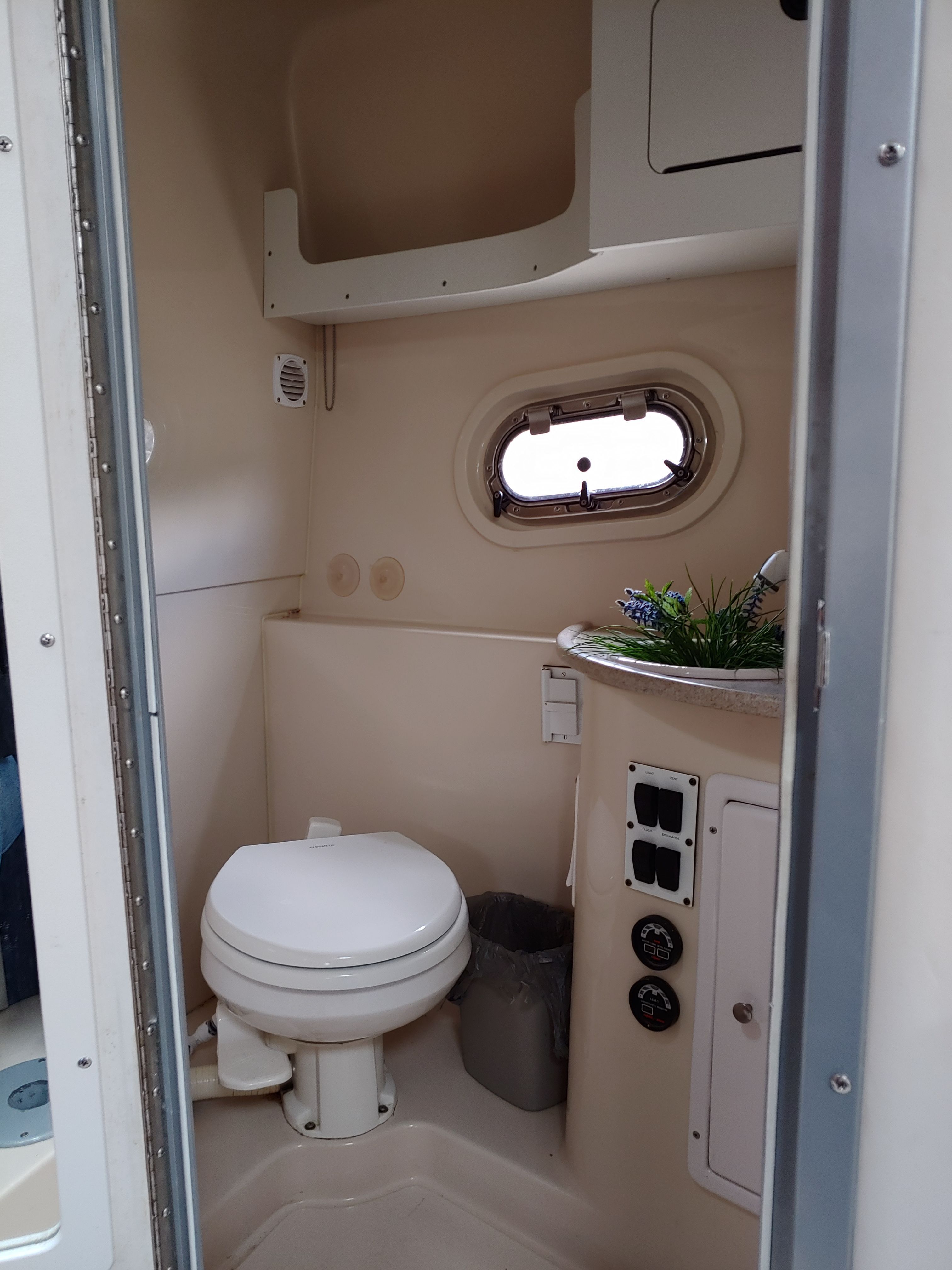 A small bathroom on a boat with a toilet, sink, and porthole.
