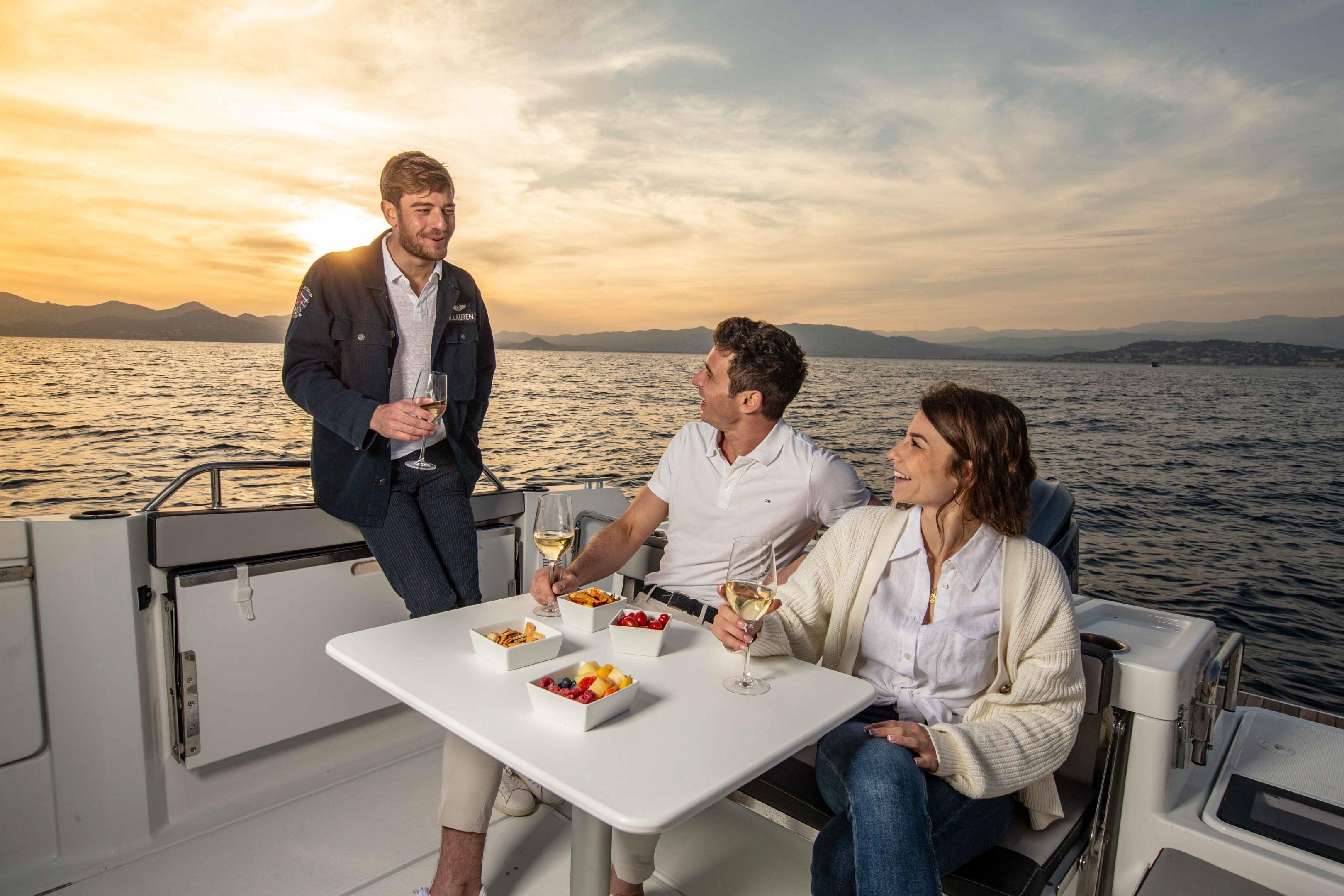 Three people enjoying drinks on a 2026 Jeanneau NC 795 Sport boat at sunset.