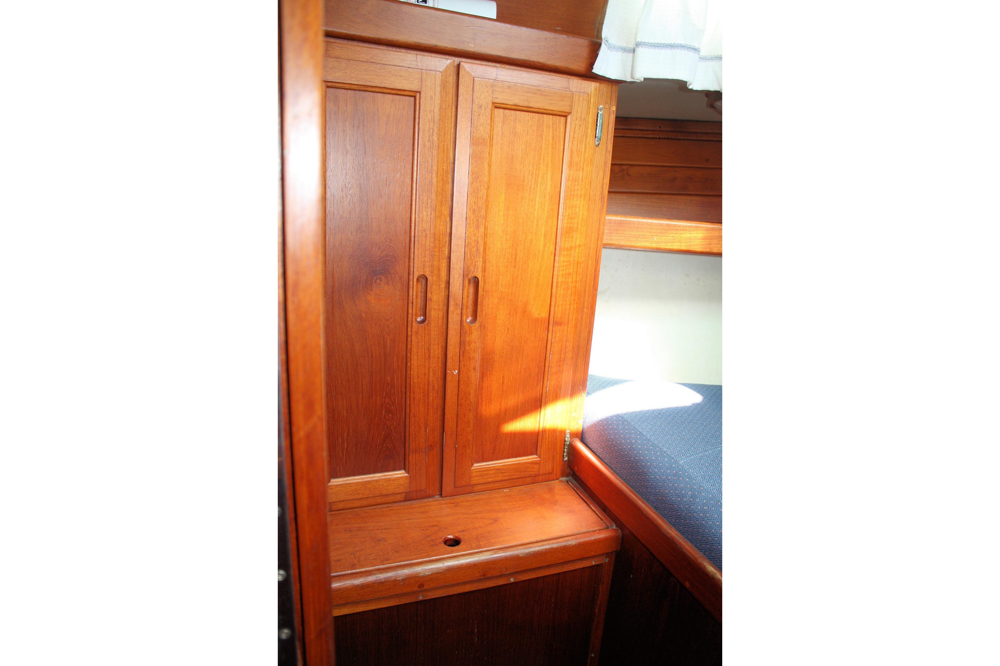 Wooden cabinet in 1987 Ericson 38-200 sailboat interior, next to a cushioned bench.