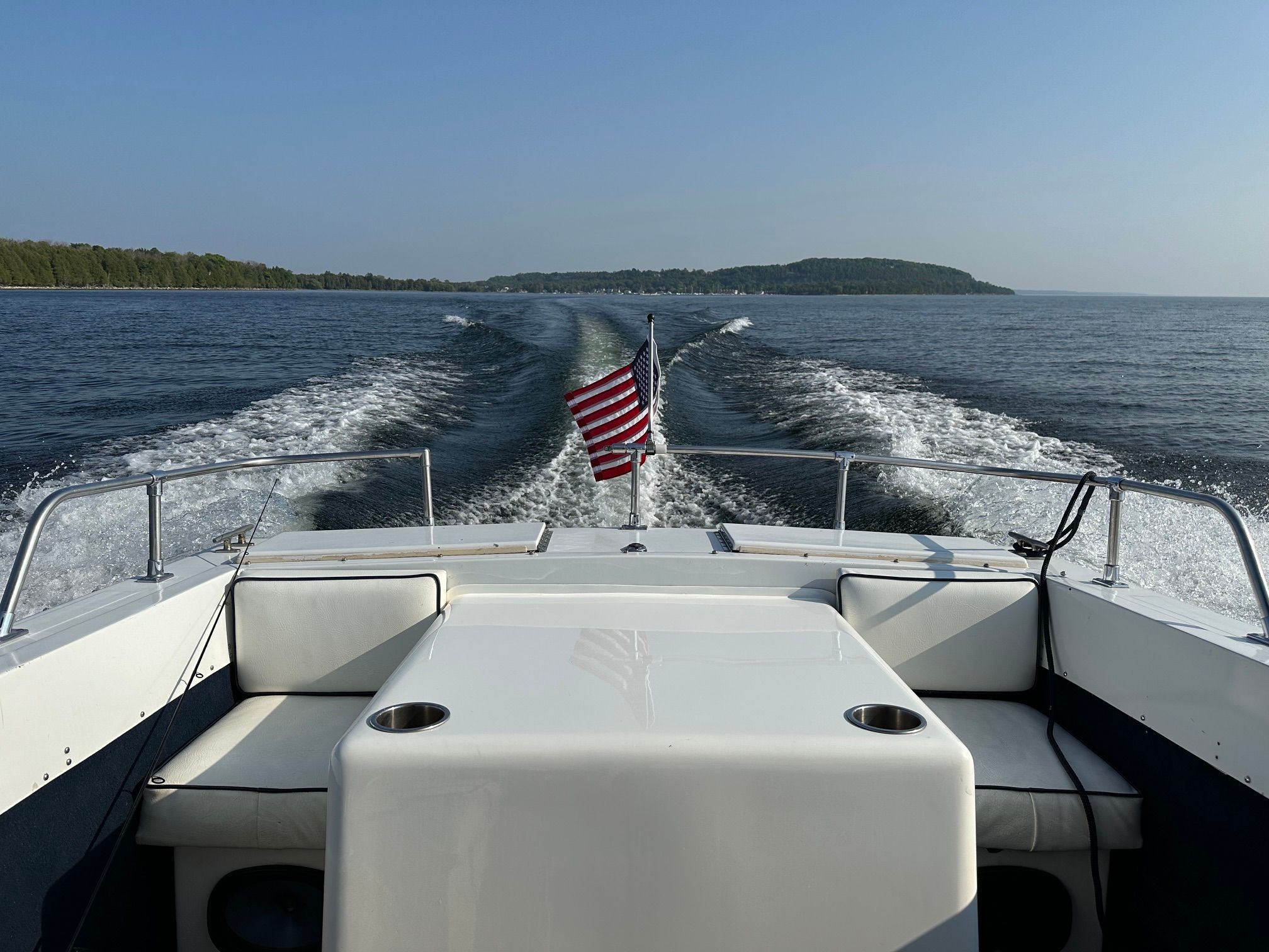 View from the stern of a boat with an American flag, cruising on calm waters.