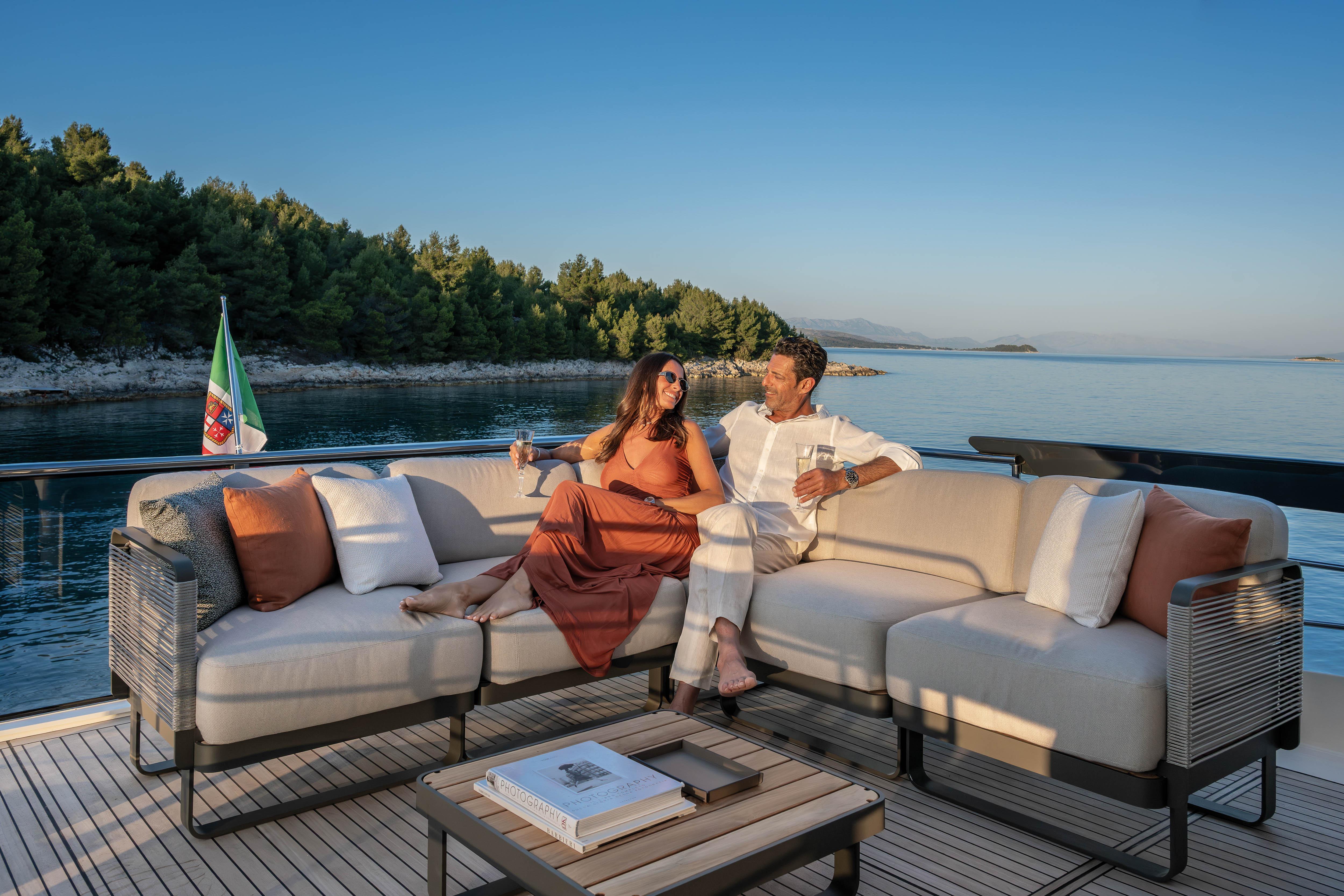 A couple relaxes on a luxurious boat overlooking the sea and coastline.
