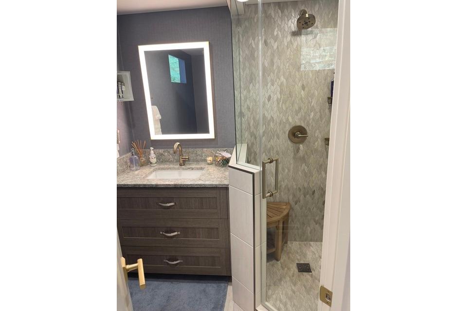 Modern bathroom with glass shower, illuminated mirror, and granite countertop, Adonia The Queen Elizabeth 2021.