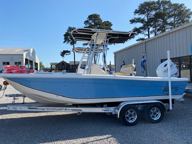 A blue 2022 Carolina Skiff 21 Ultra Elite boat on a trailer beside a building.