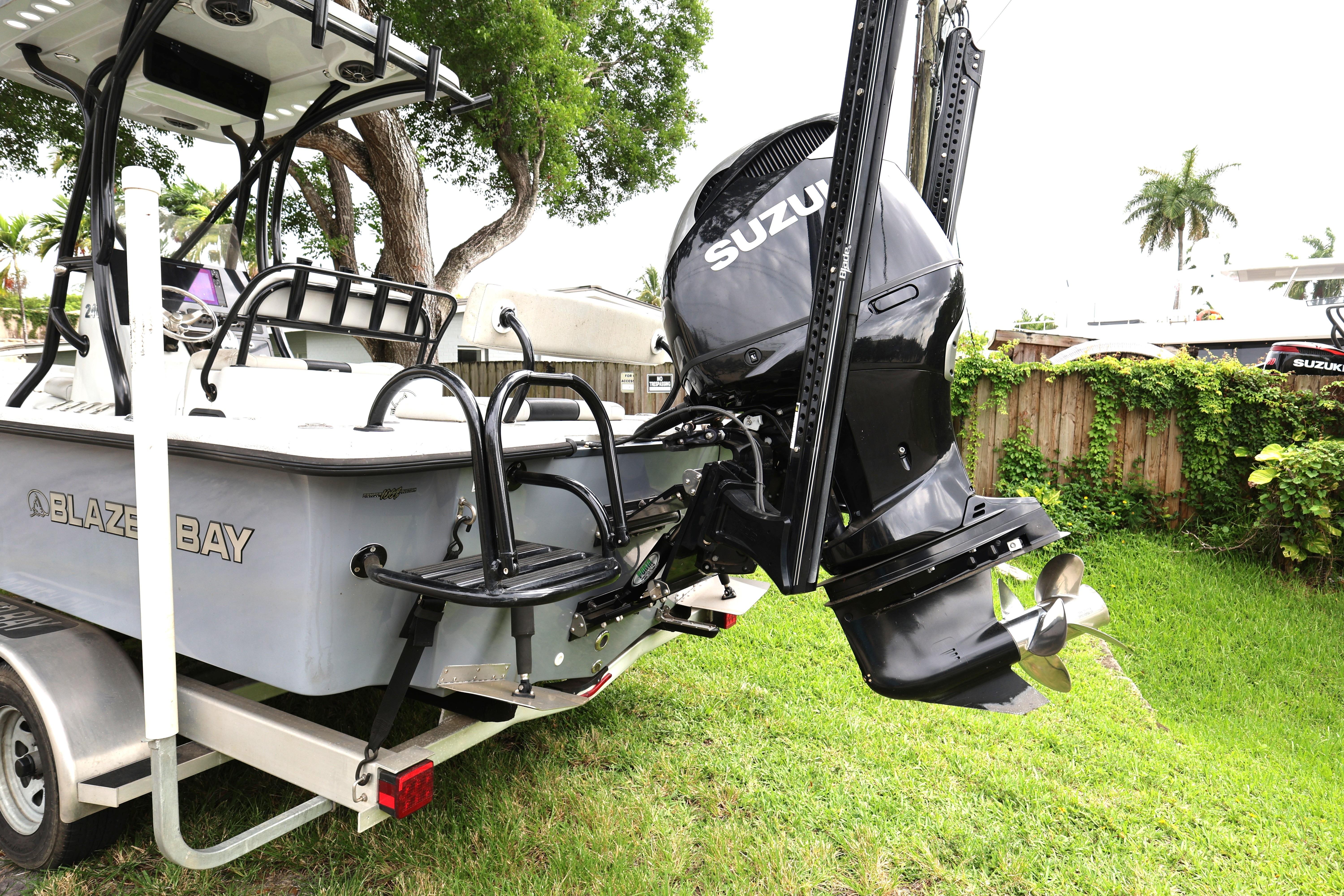 2021 Blazer Bay 2400 boat with Suzuki outboard motor on trailer, parked in a lush yard.