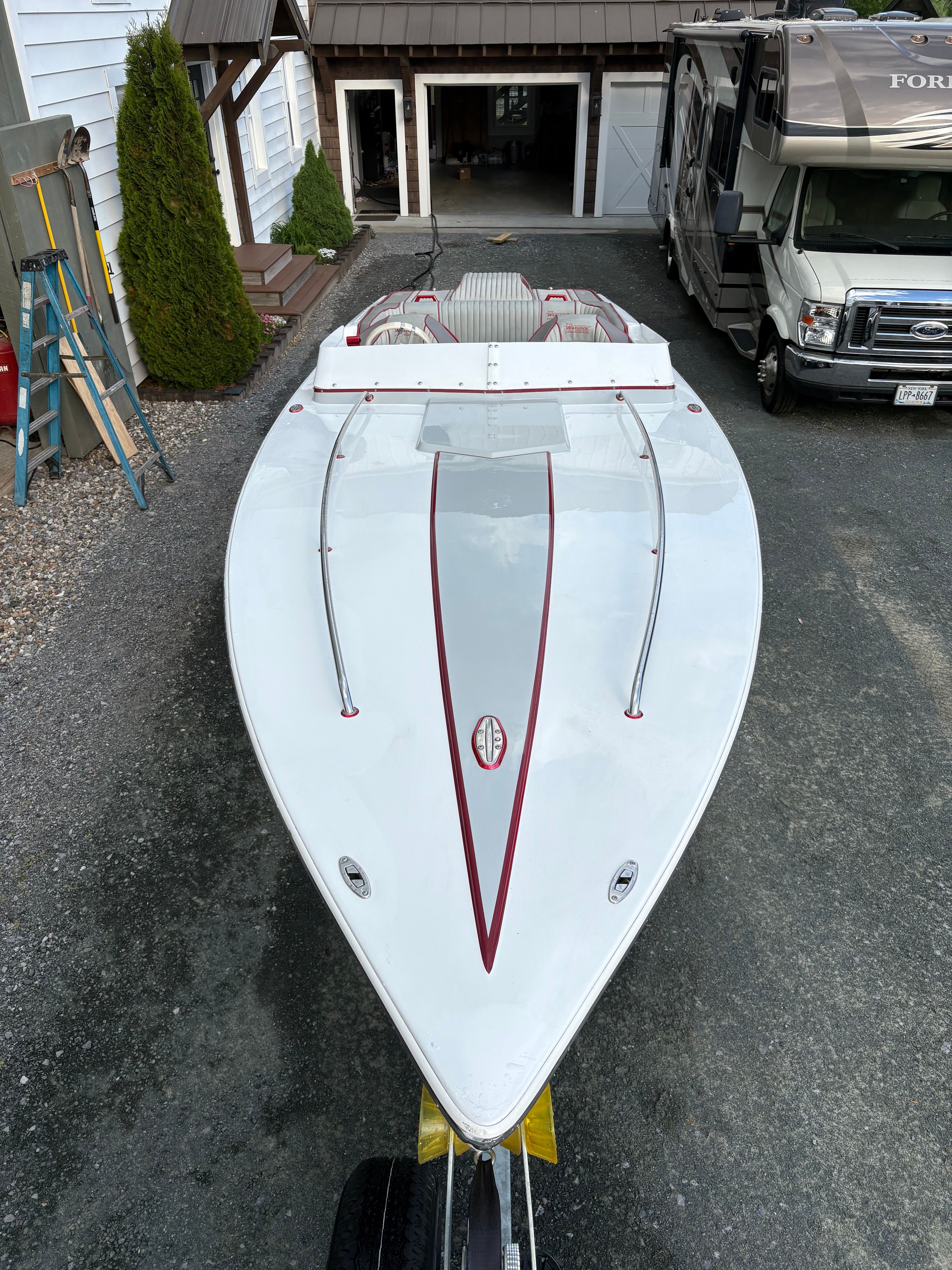 A white boat with red stripes is on a trailer in a driveway.