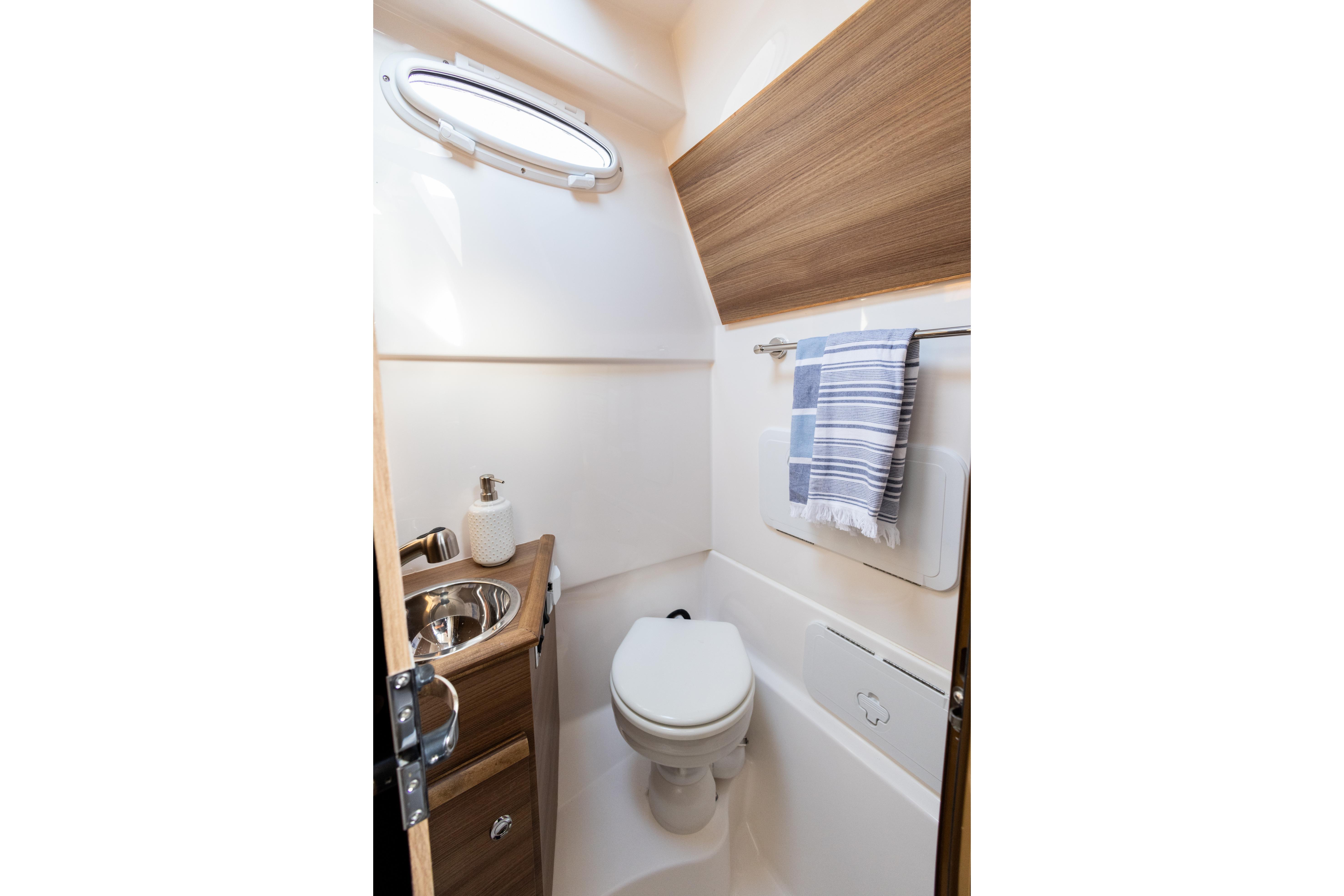 Compact bathroom in 2025 Solara S-310 CW boat with sink, toilet, and towel rack.