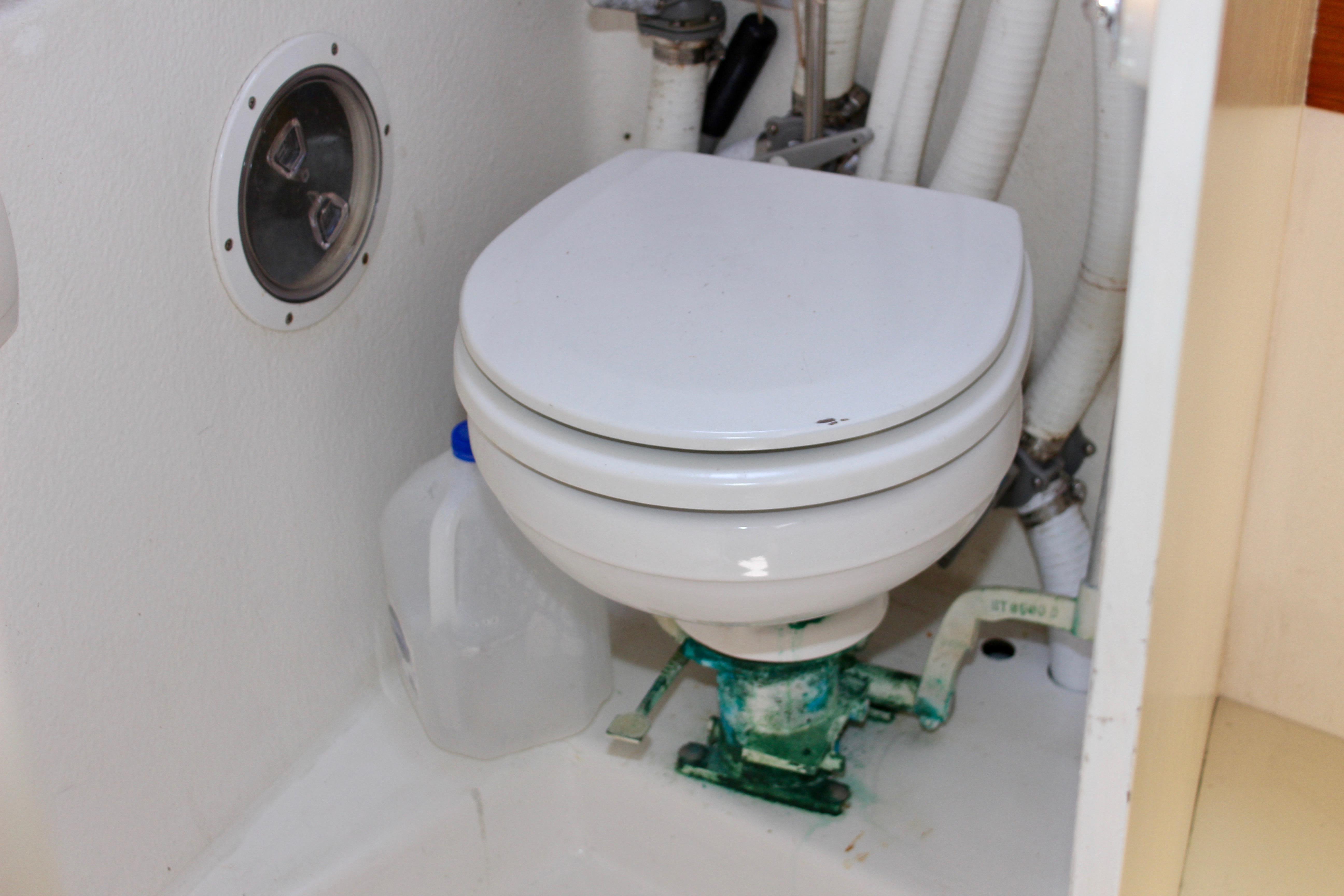 Marine toilet in a 1993 Freya 39 sailboat bathroom, with plumbing and a water jug.