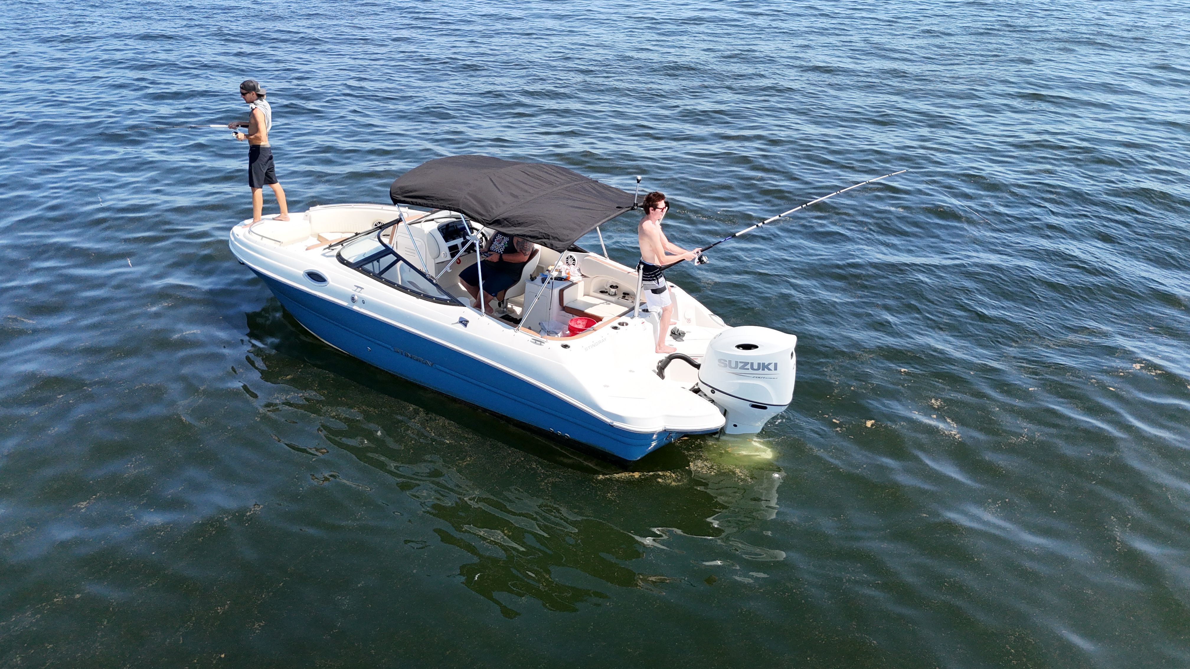Two people are fishing on a boat in open water.