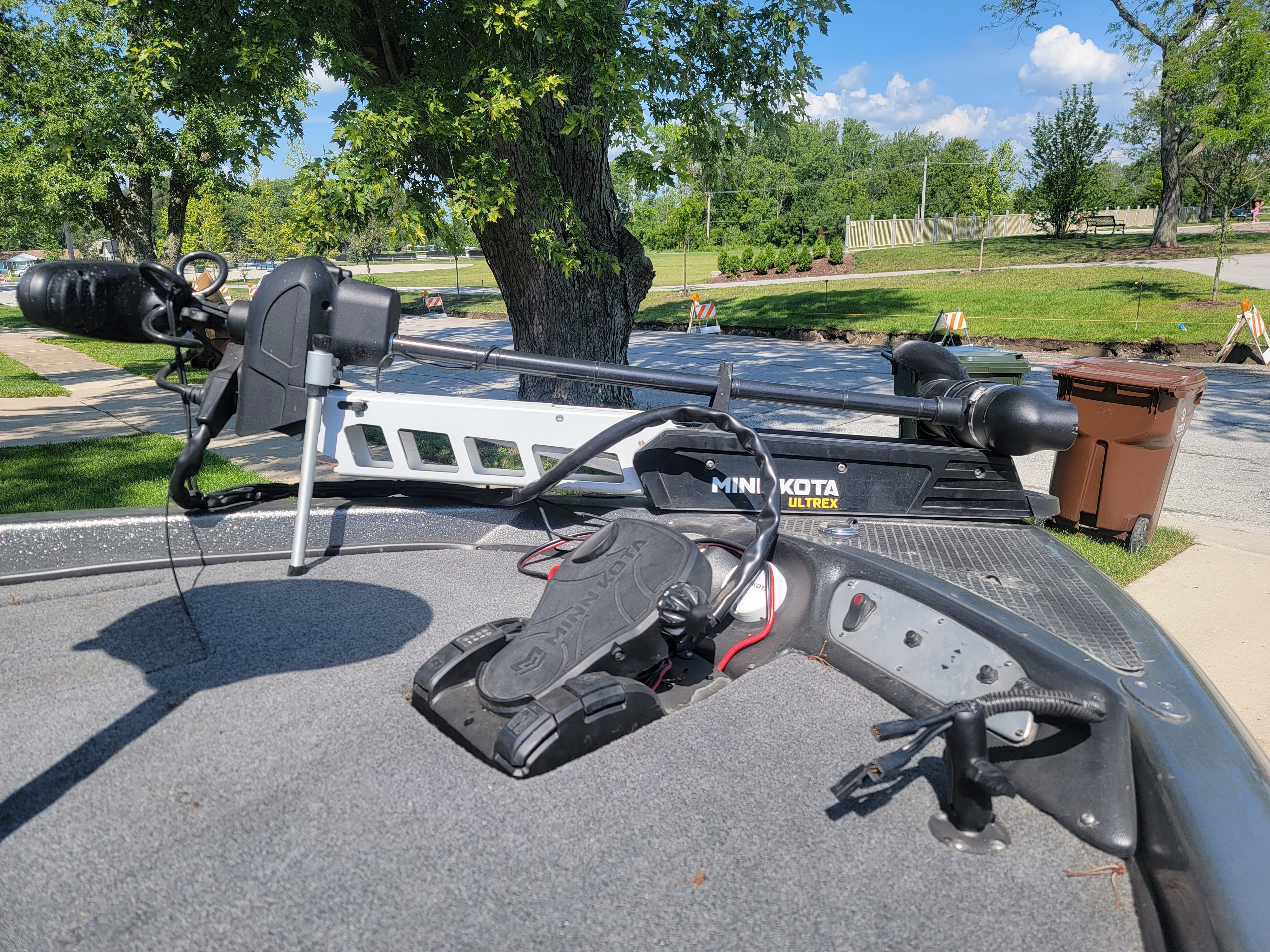 A boat with a Minn Kota trolling motor on a gray deck, surrounded by trees.
