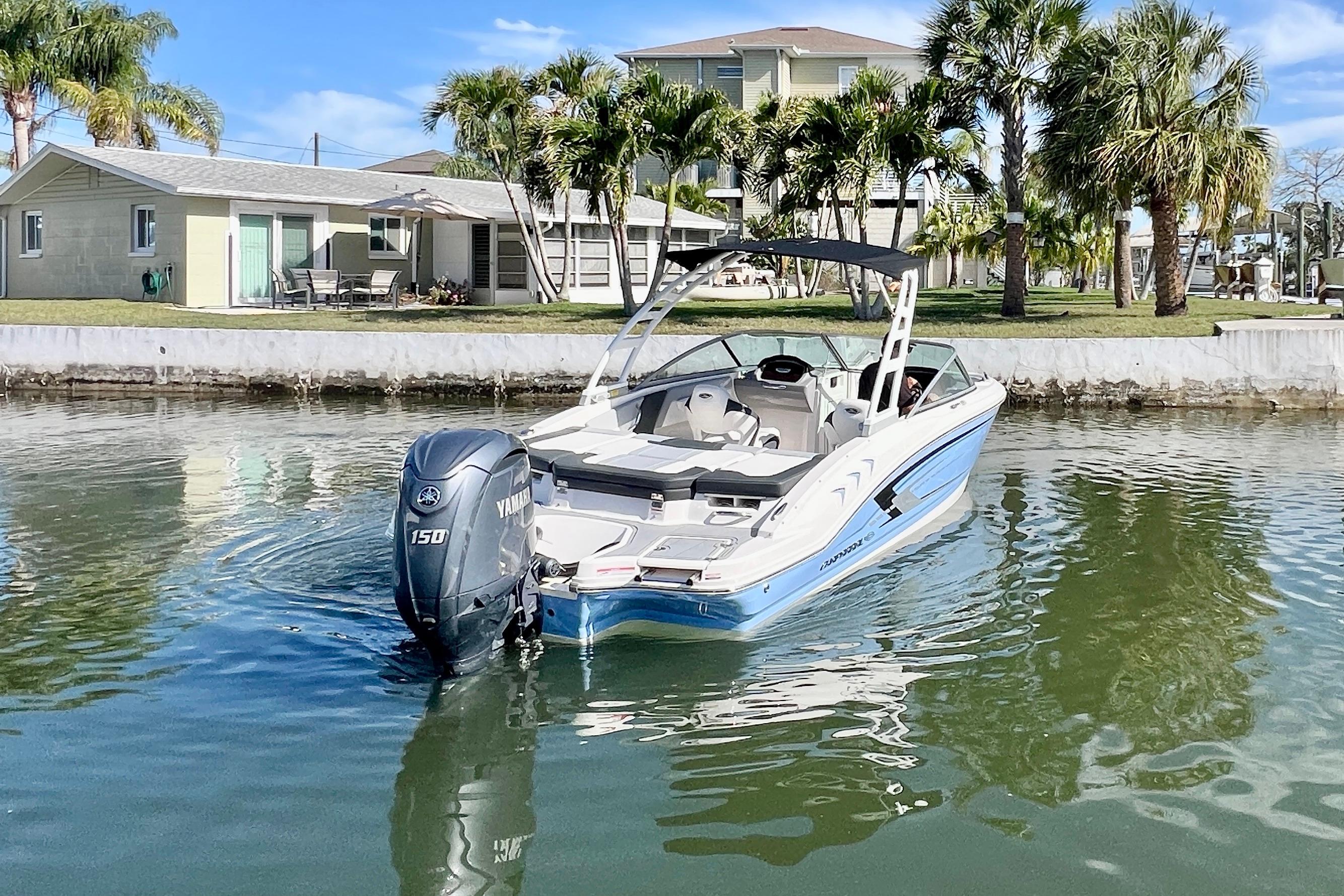 2023 Chaparral 21 SSi OB boat on calm water near a tropical waterfront home.