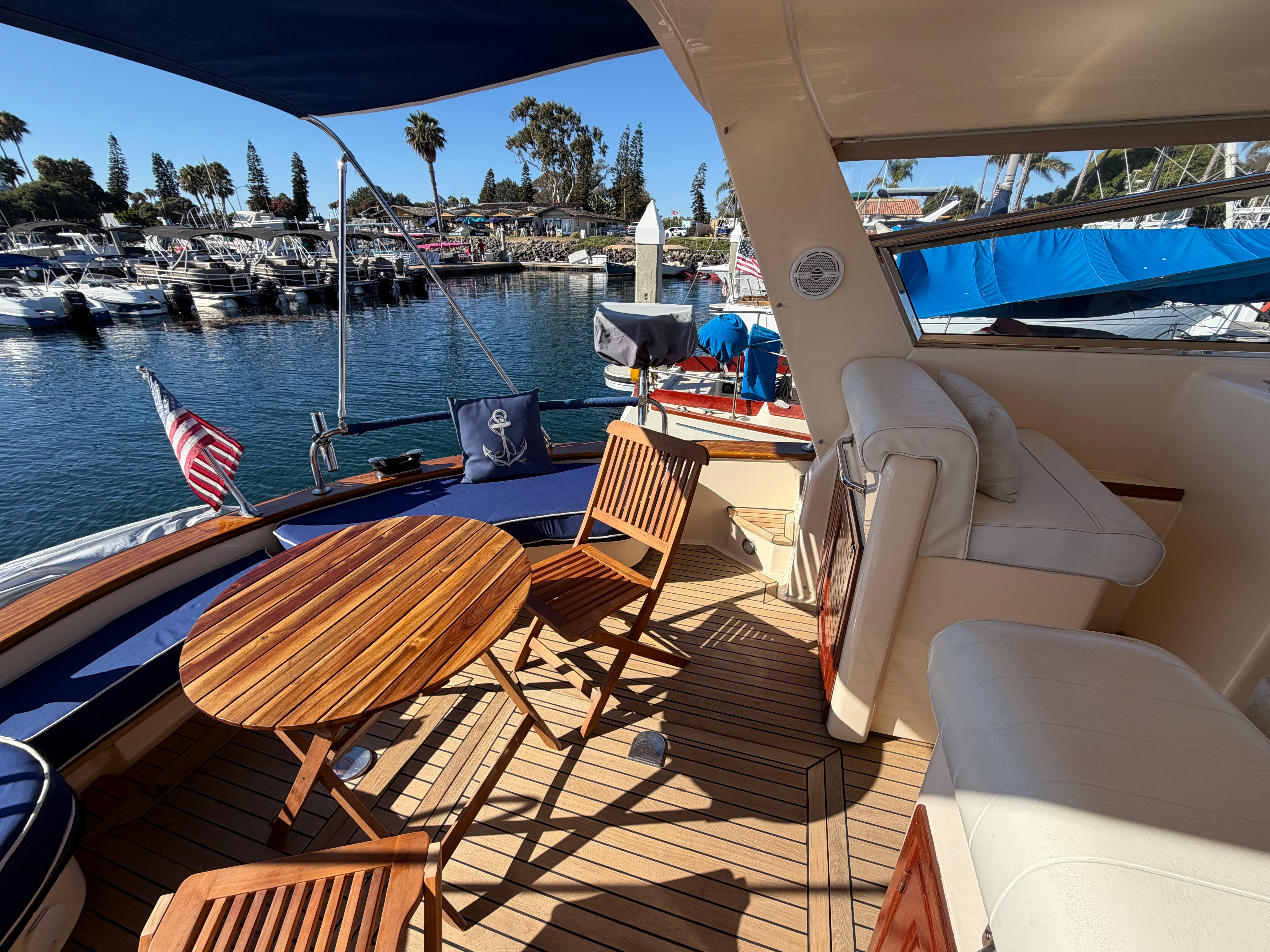 The image shows the deck of a 2003 Apreamare 11 with wooden furniture and a view of the marina.