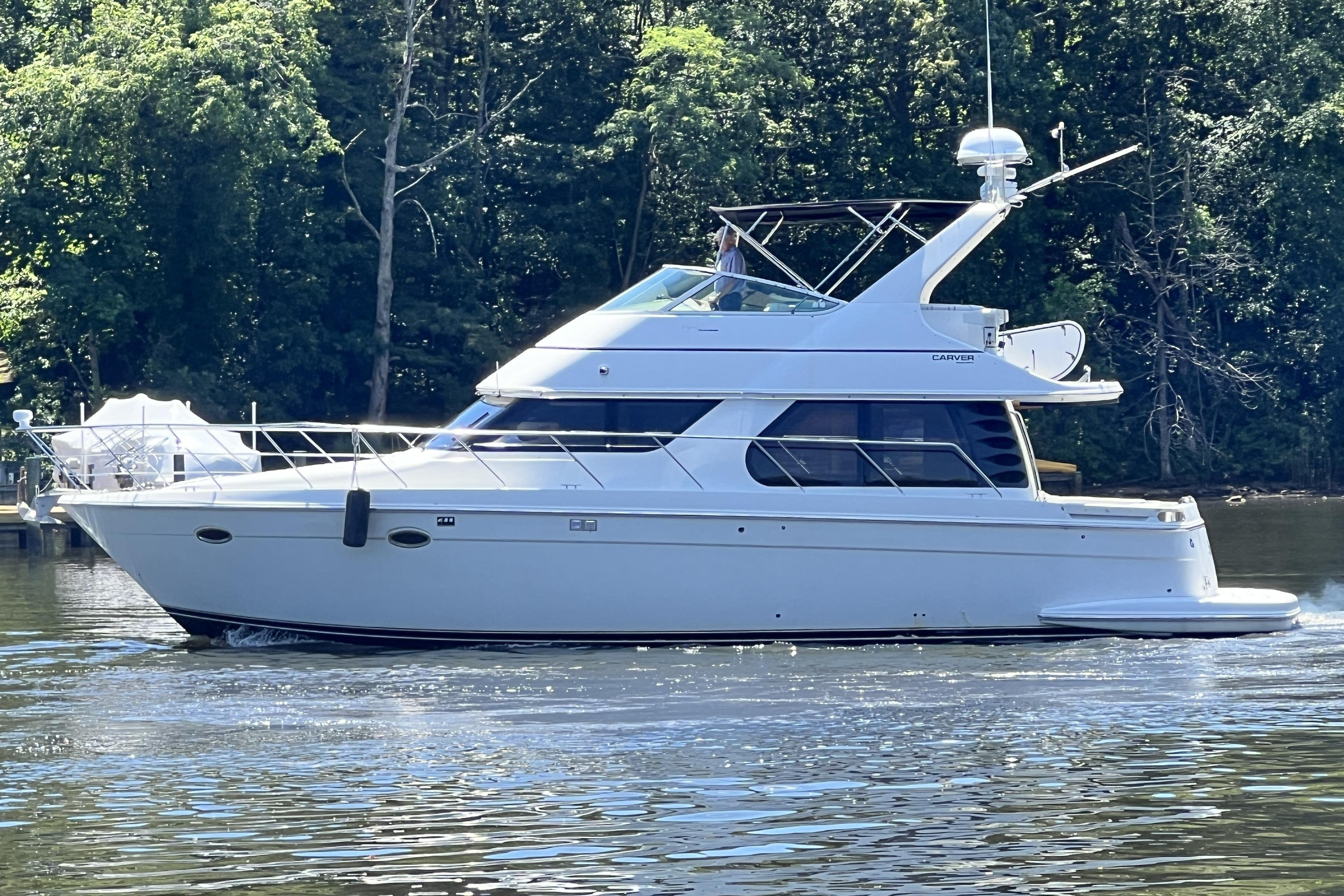 2003 Carver 450 Voyager Pilothouse yacht cruising on a serene lake with lush forest backdrop.
