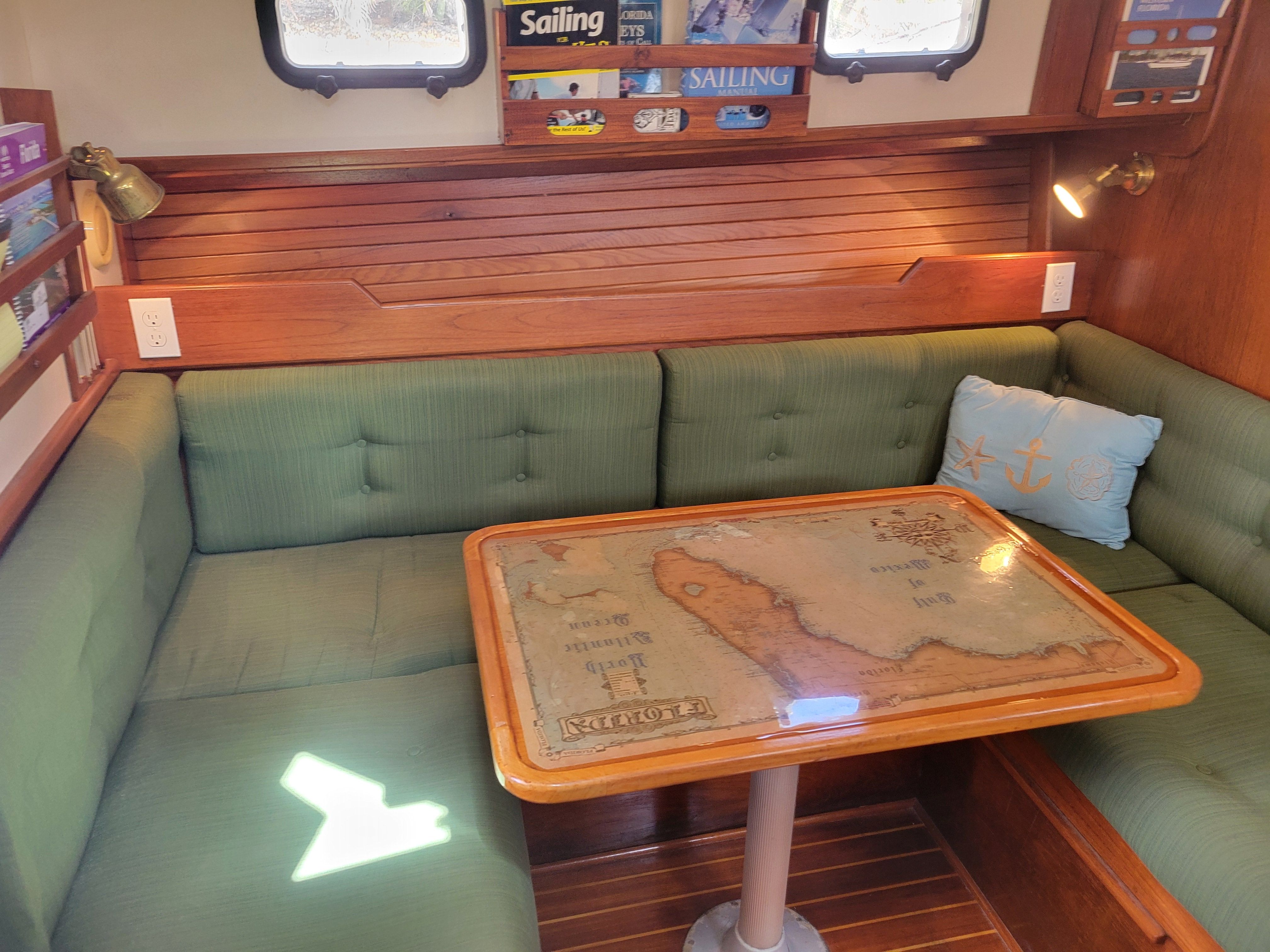 Interior of a 1989 Cape Dory MS300 with green sofa and wooden table featuring a nautical chart.