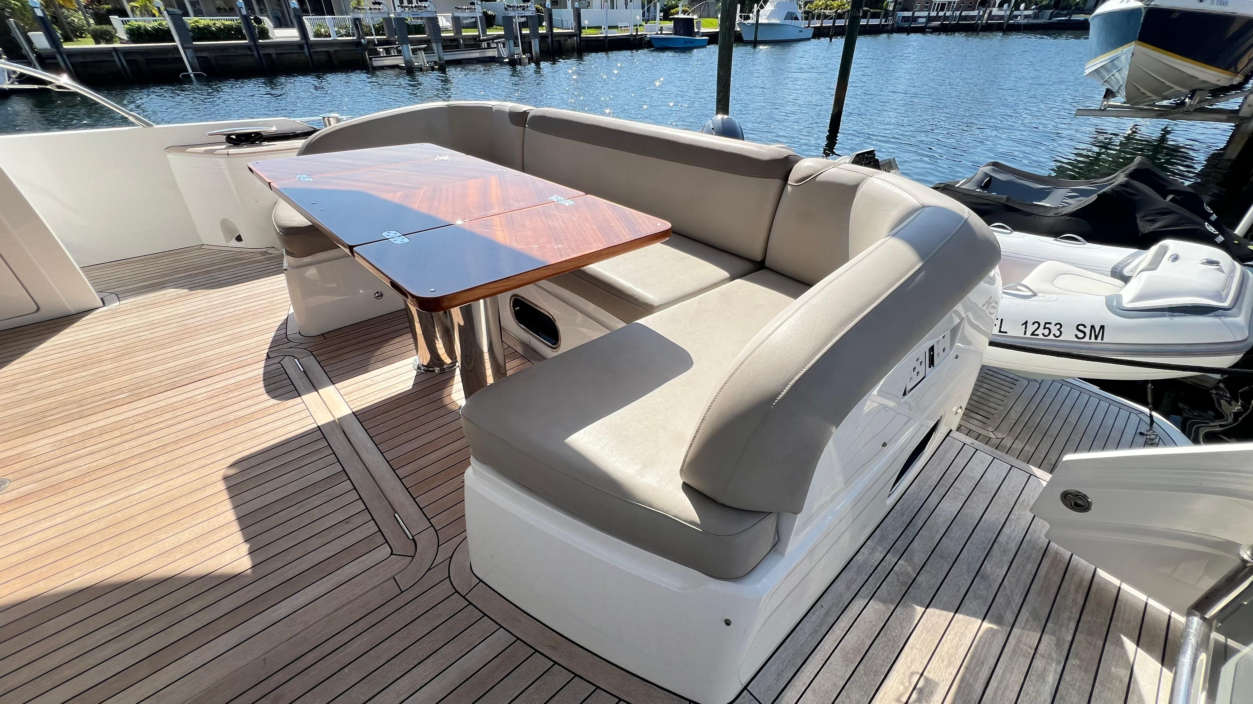 Luxurious seating area on 2019 Princess F62 yacht with wooden table, docked by the water.
