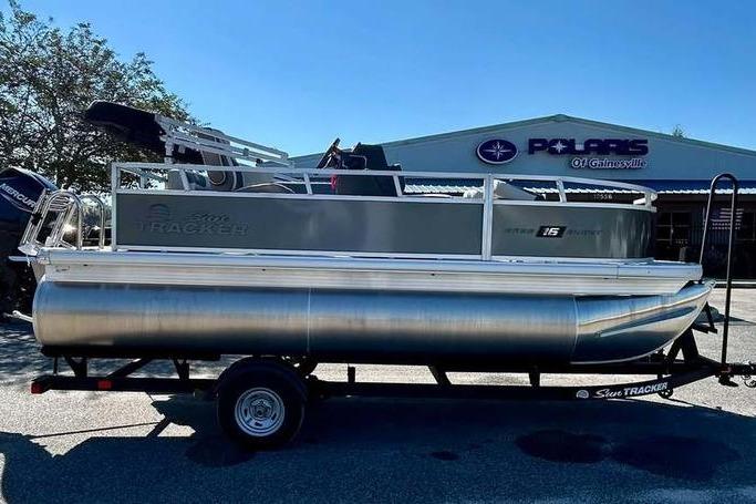 2026 Sun Tracker Bass Buggy 16 XL Select pontoon boat on trailer, parked outside dealership.