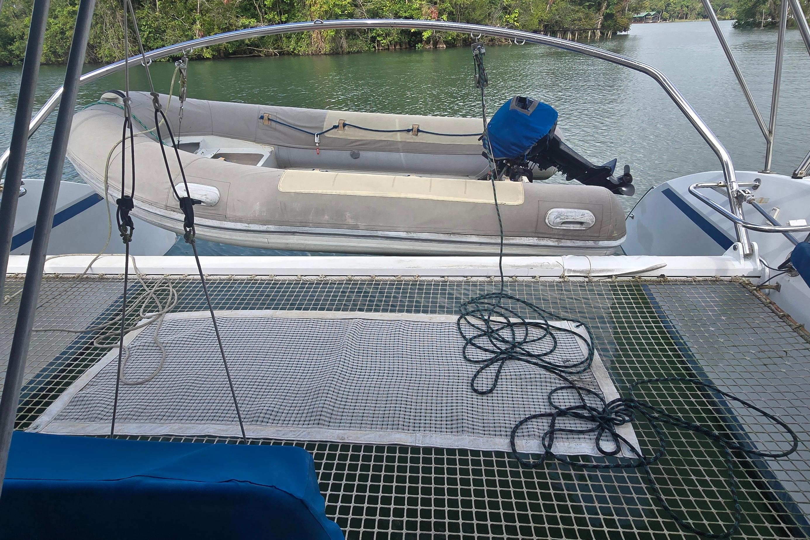 Catamaran deck with netting, inflatable boat, and scenic water view. Naval Force 3 Tropic 56, 1997.
