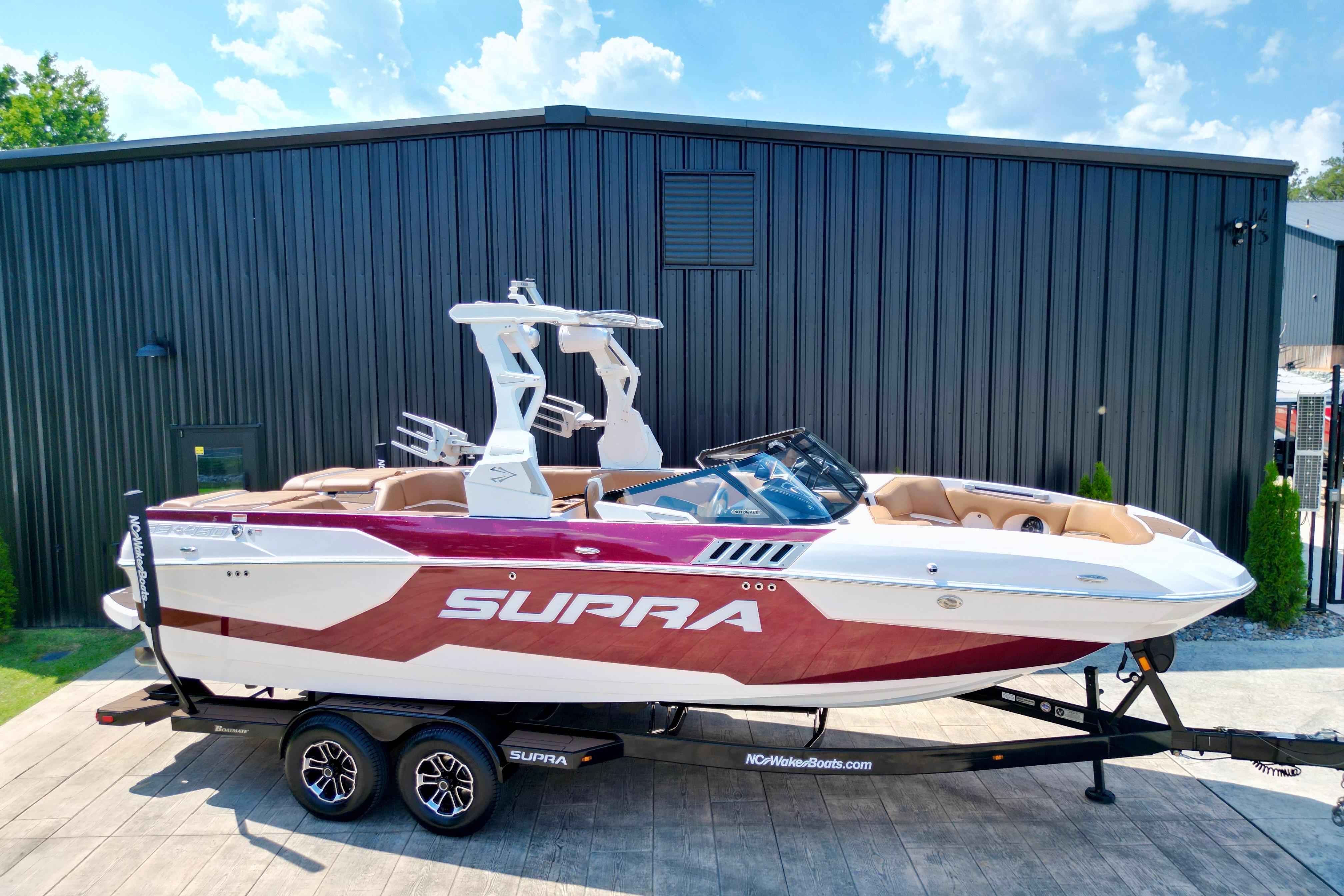 2021 Supra SE boat with sleek design, parked on a trailer, against a modern building backdrop.