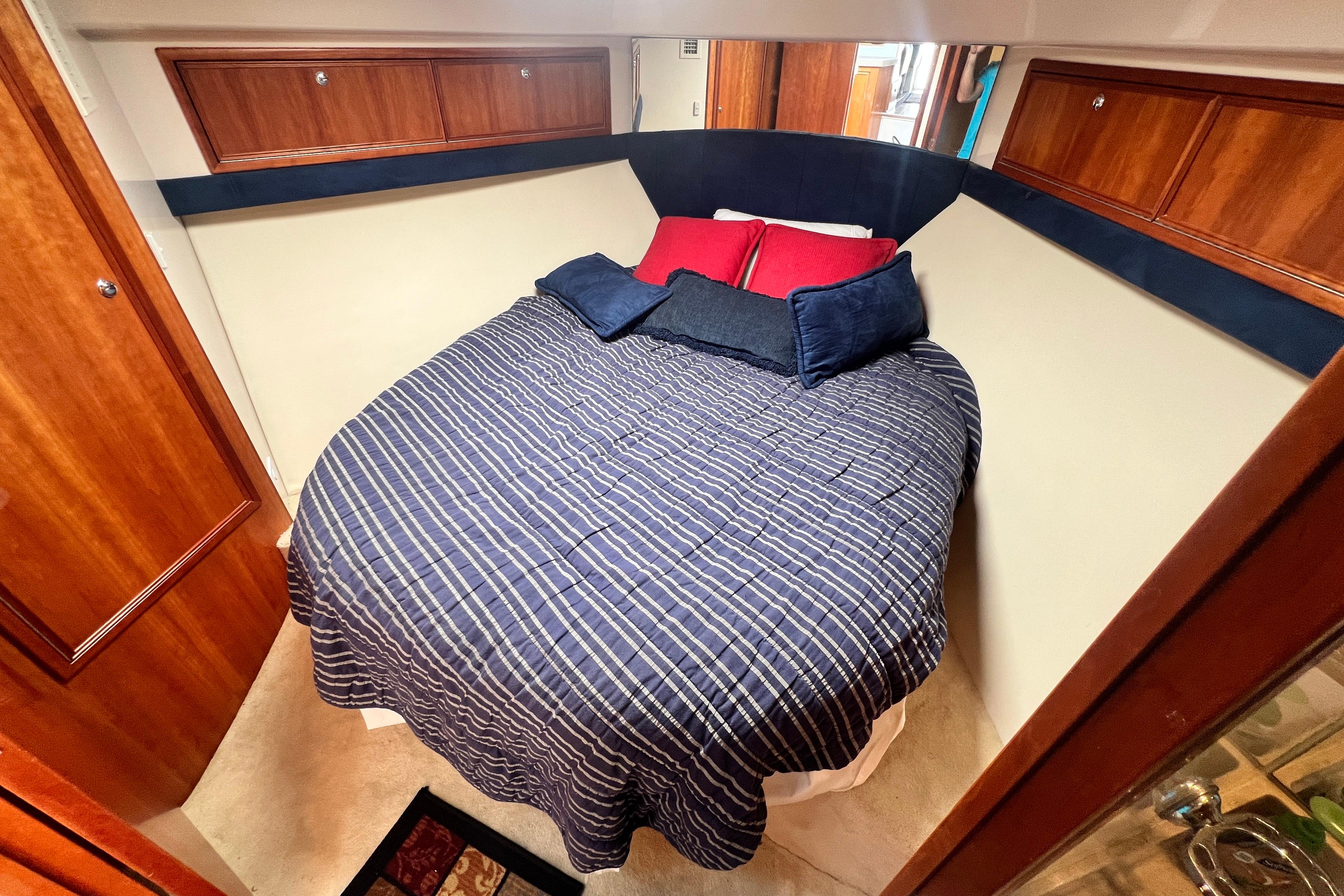 Cozy bedroom in 2007 Riviera 33 Flybridge yacht with striped bedding and wooden cabinets.