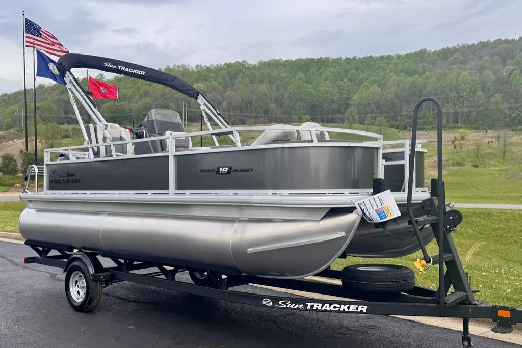 2026 Sun Tracker Bass Buggy 18 DLX pontoon boat on trailer, flags in background.