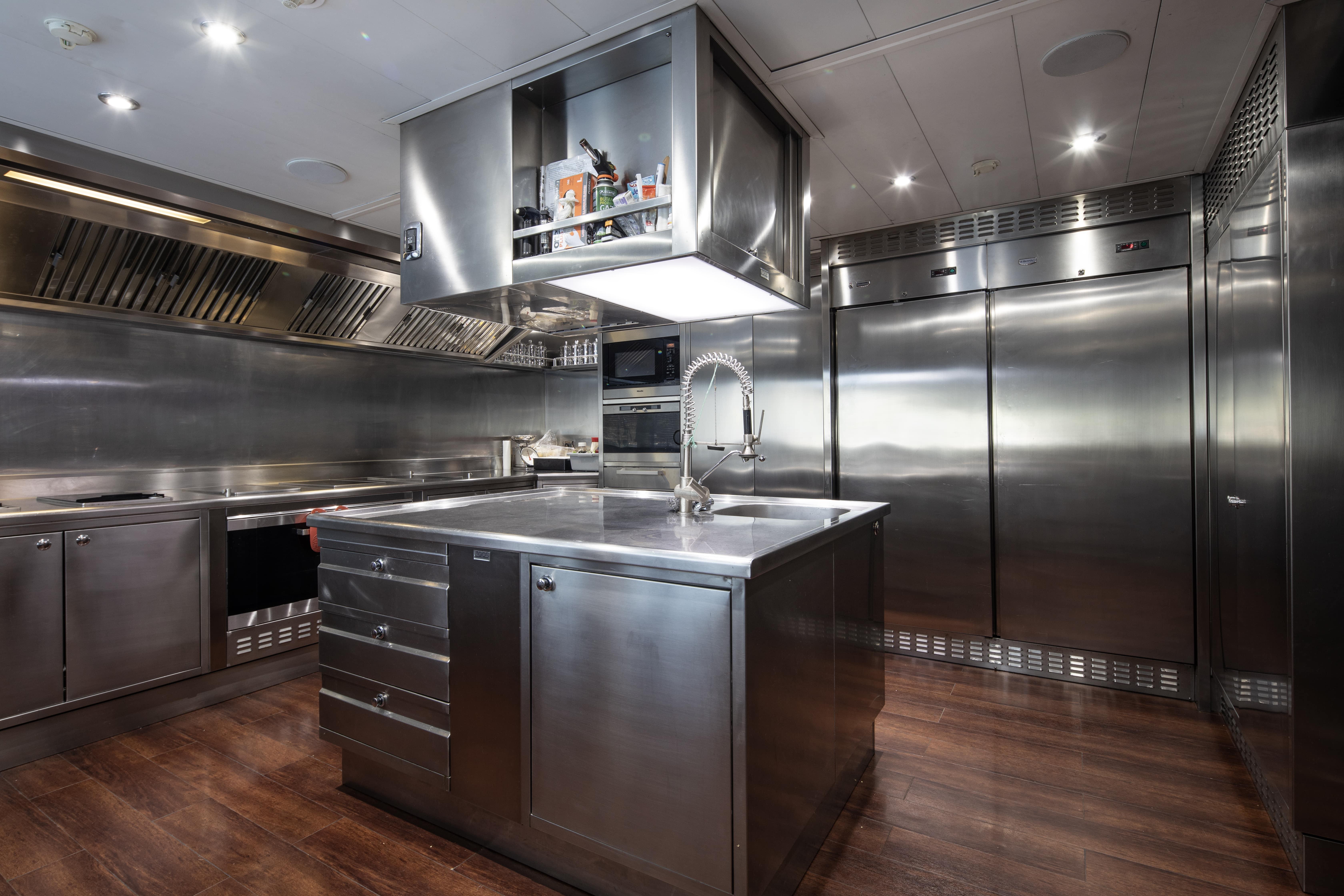 Modern stainless steel kitchen with island, professional appliances, and wooden flooring on a CRN 185 yacht.