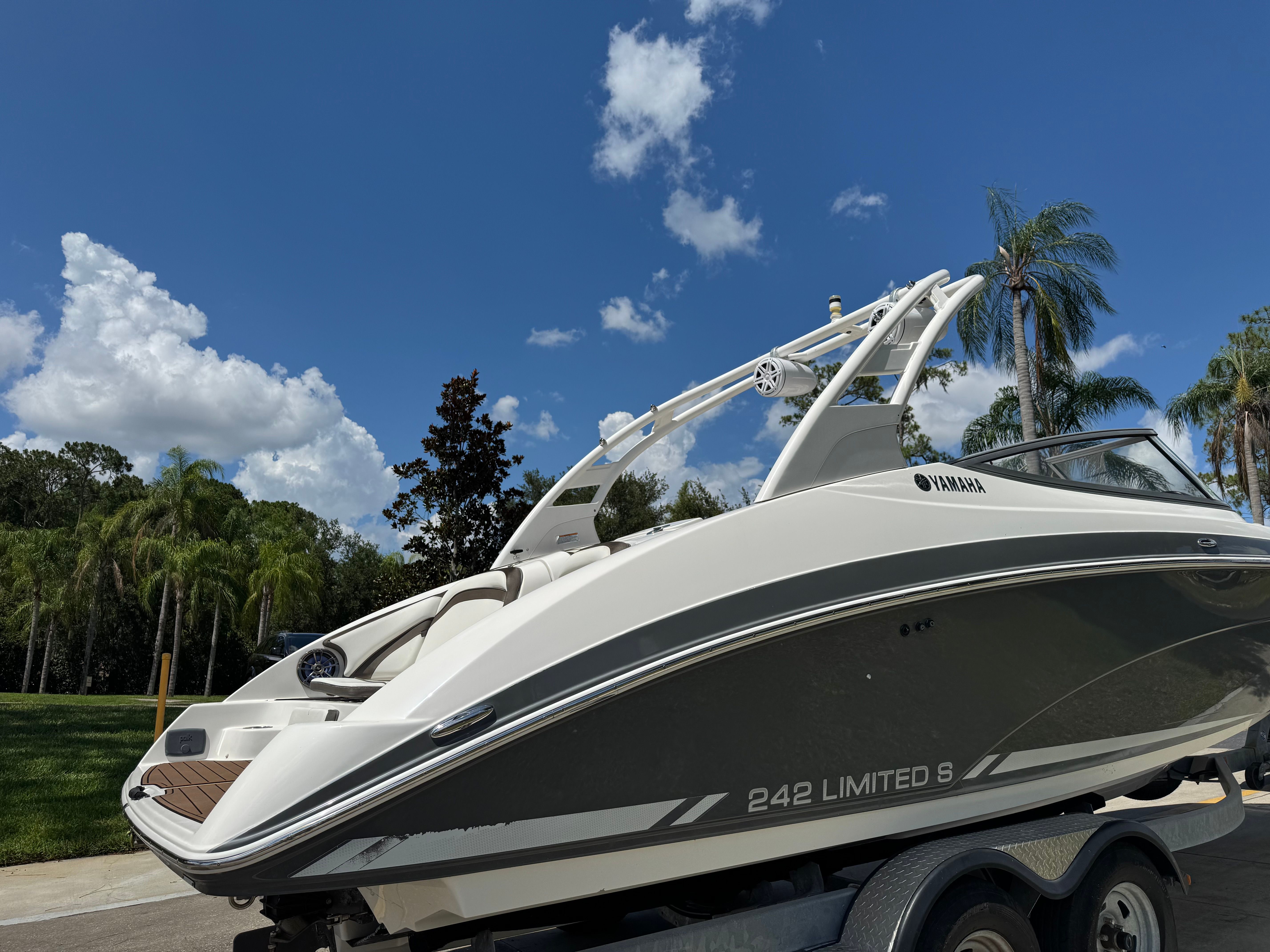 A 2015 Yamaha 242 Limited S boat on a trailer, surrounded by palm trees and blue sky.