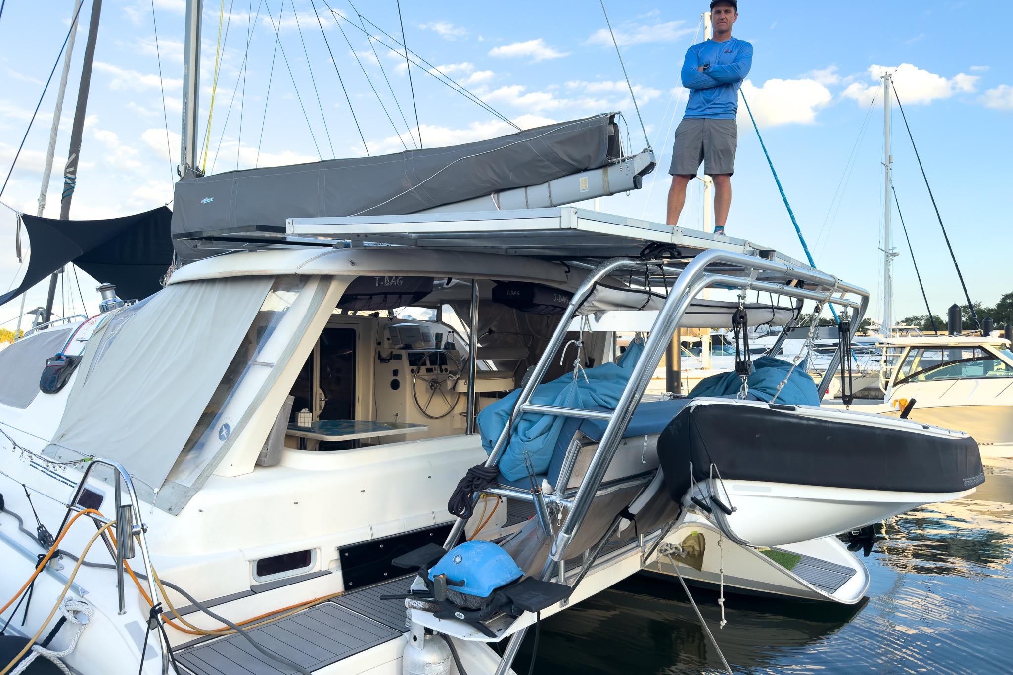 Man standing on 2006 Leopard 43 catamaran at marina, with dinghy and clear sky.